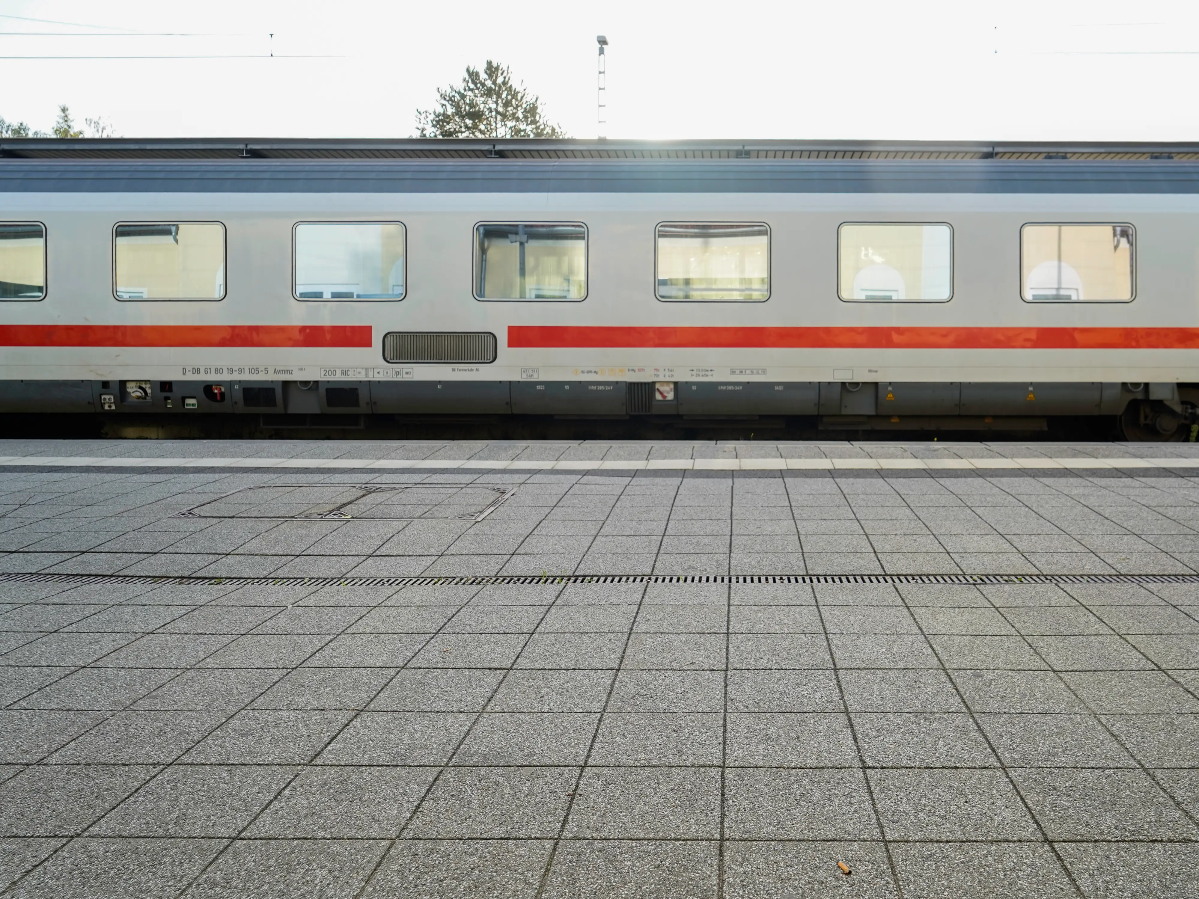 A gray train with a red strip parked at an outdoor platform