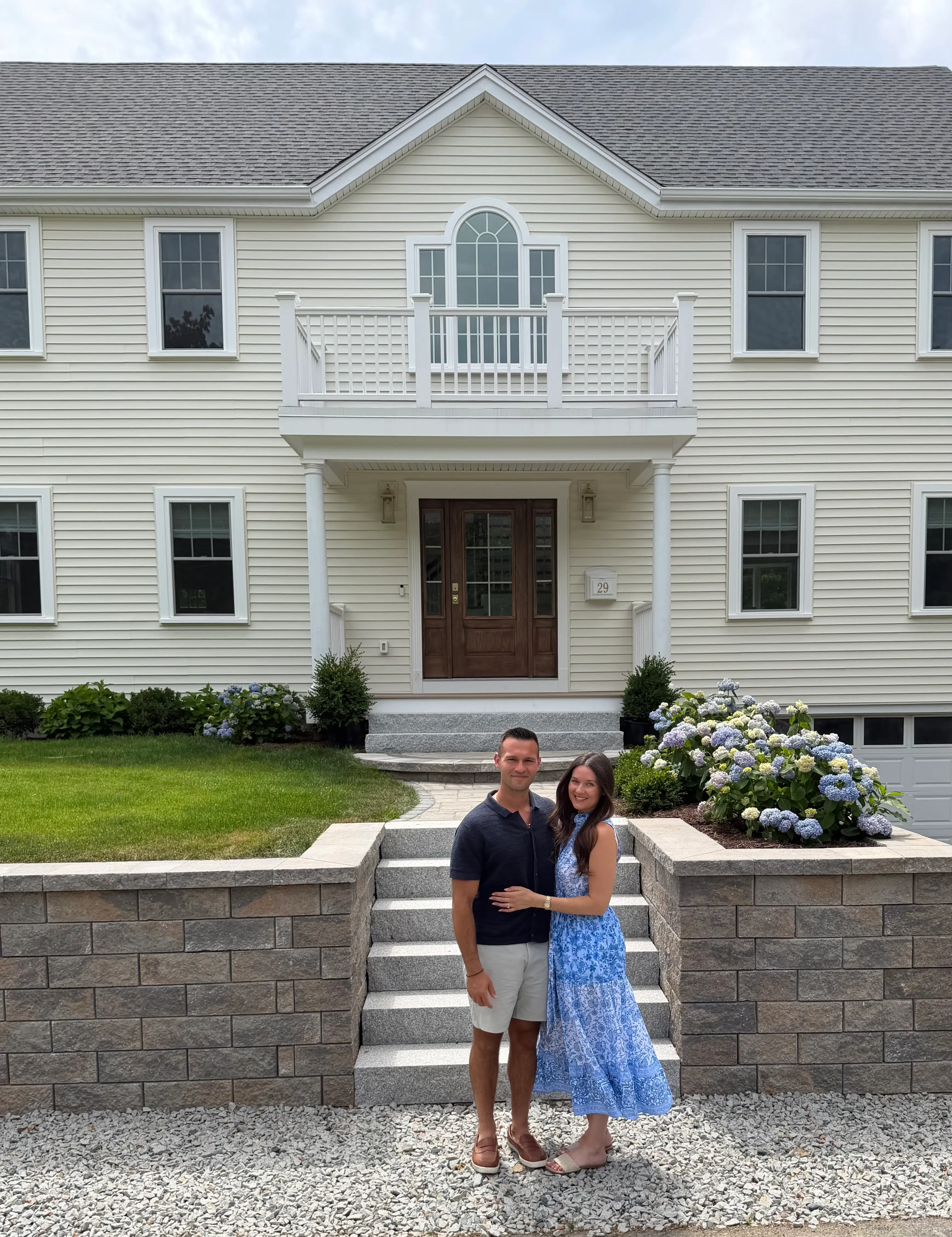 A couple stands in front of their colonial home.