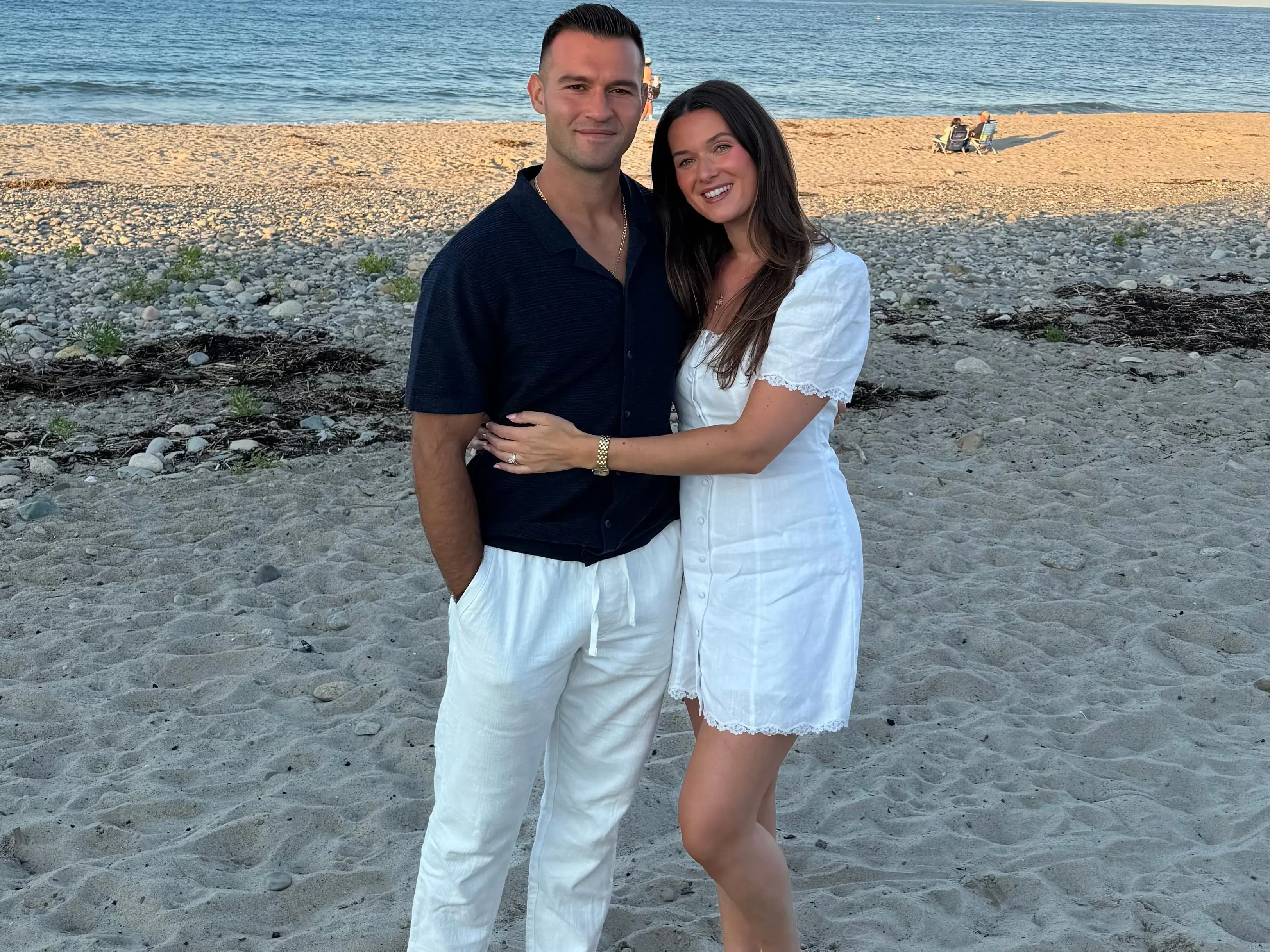 A couple leans together and smiles on a beach.
