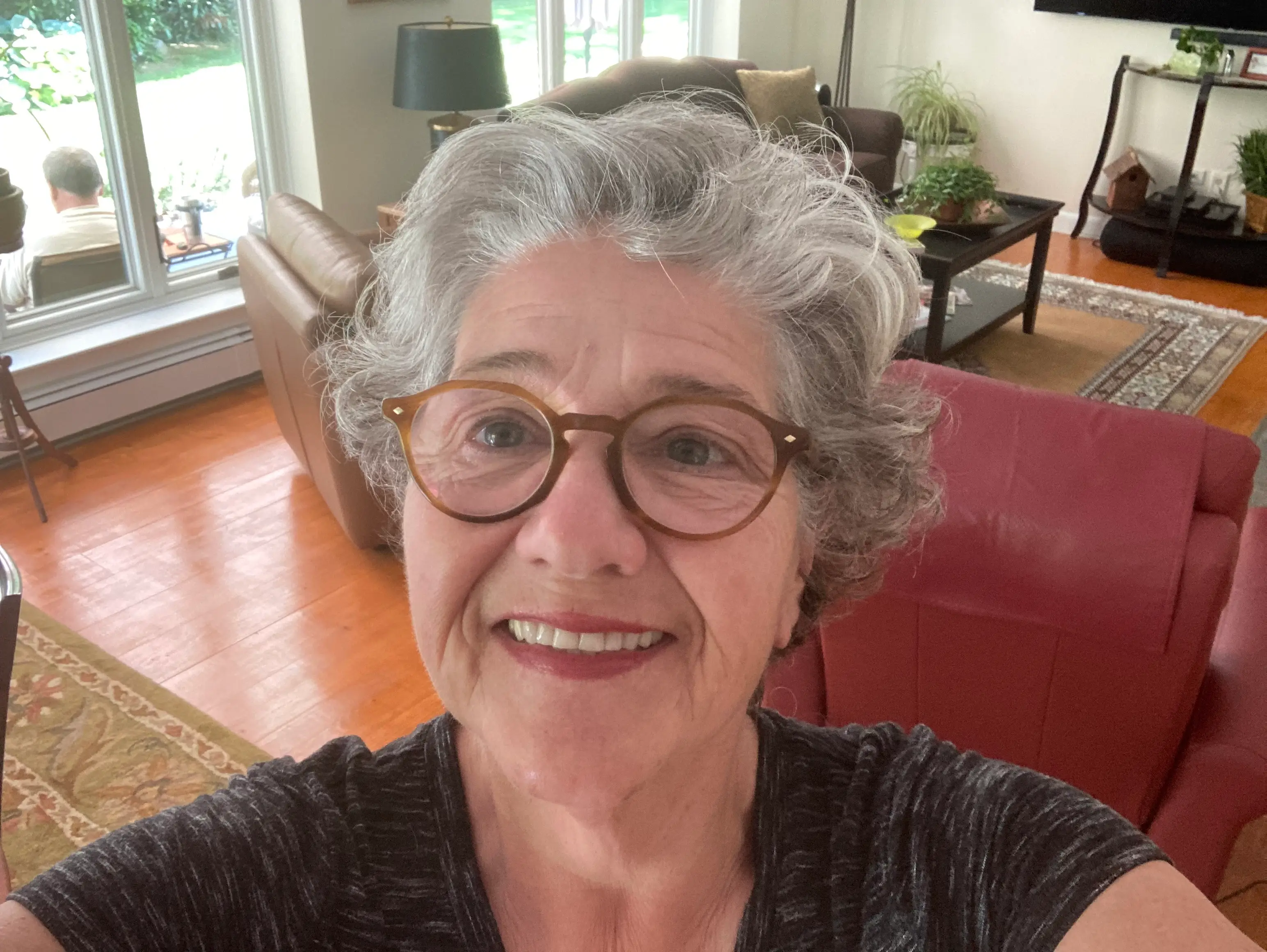 A woman, Feliz Hebert, smiles at a camera while in her living room.