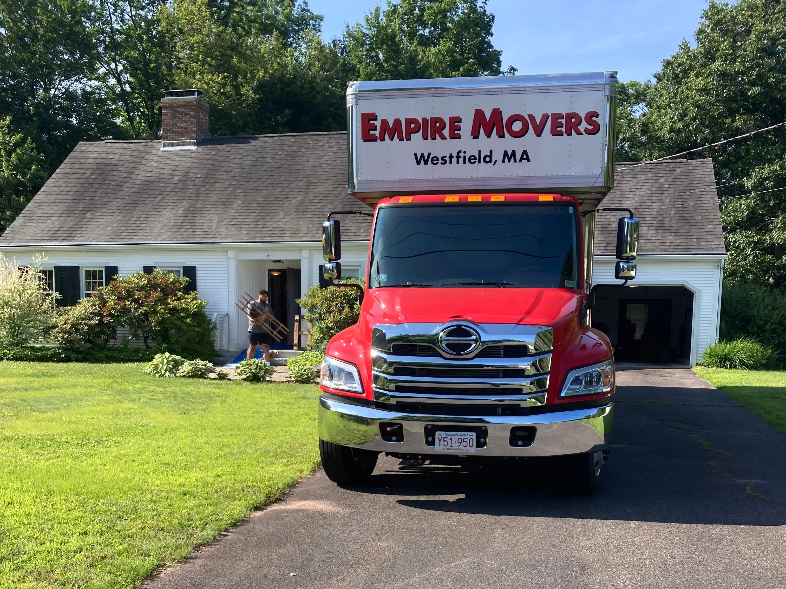 Empire Movers truck parked in a residential driveway outside a white house on a sunny day.