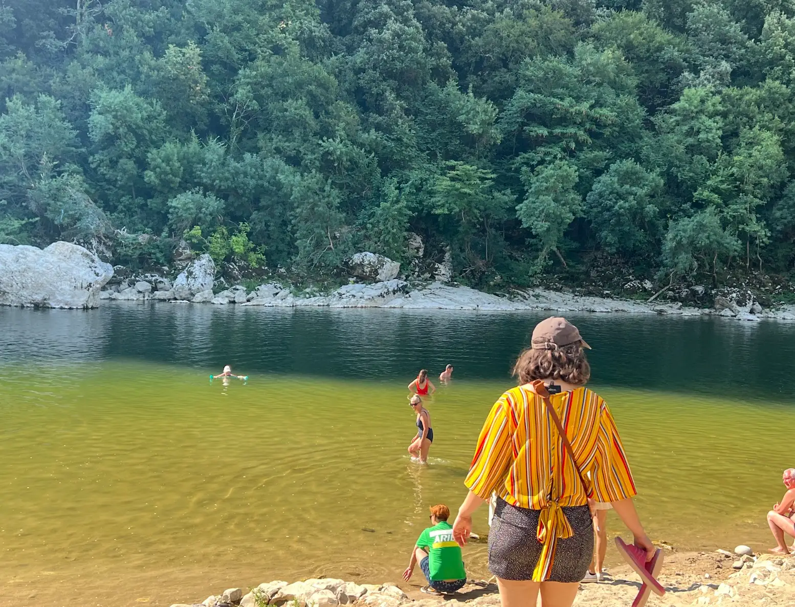 The writer walking toward a blue-green body of water, with trees in the background.