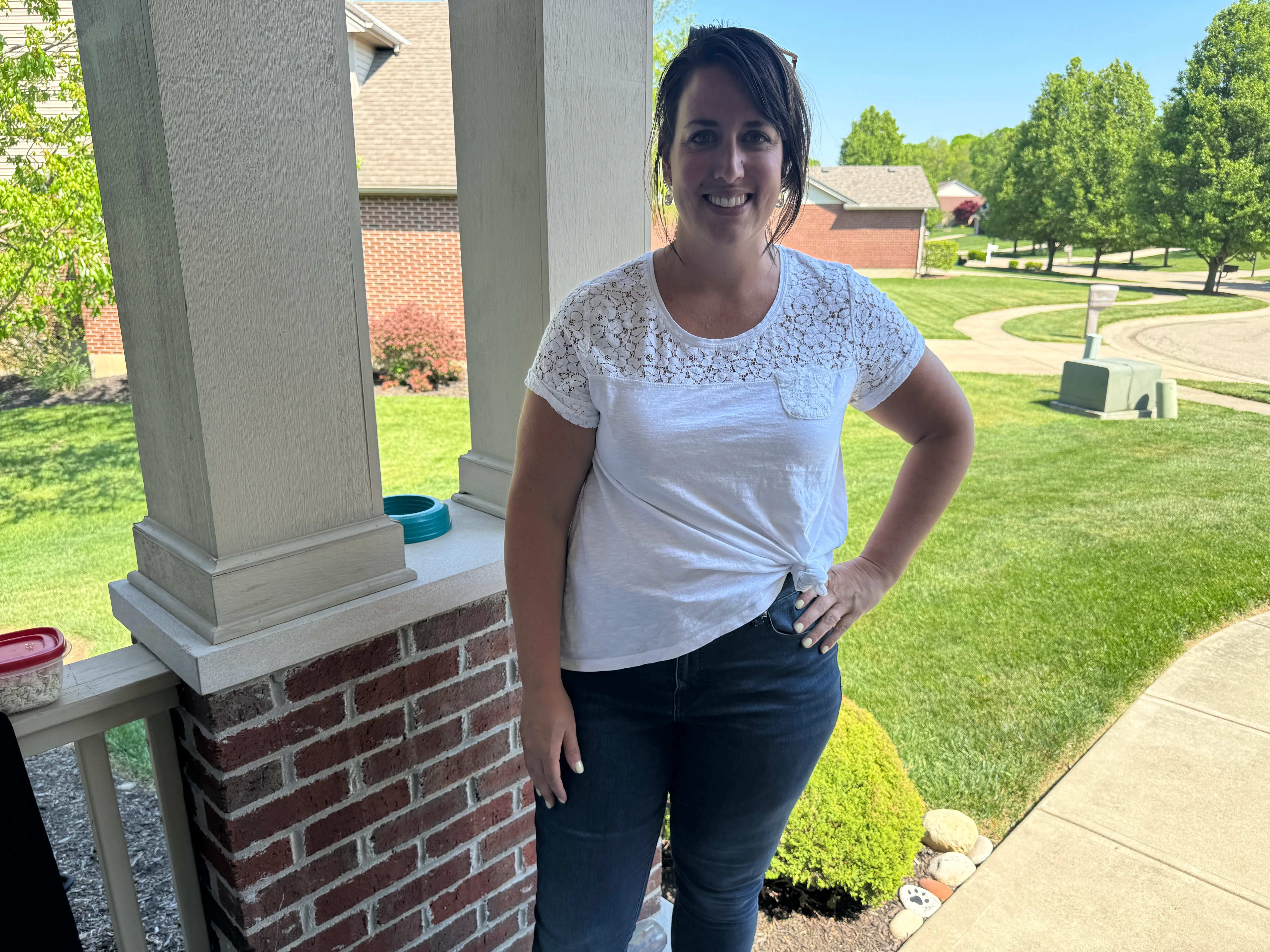 Woman in white shirt, black pants posing in front of garage and brick wall