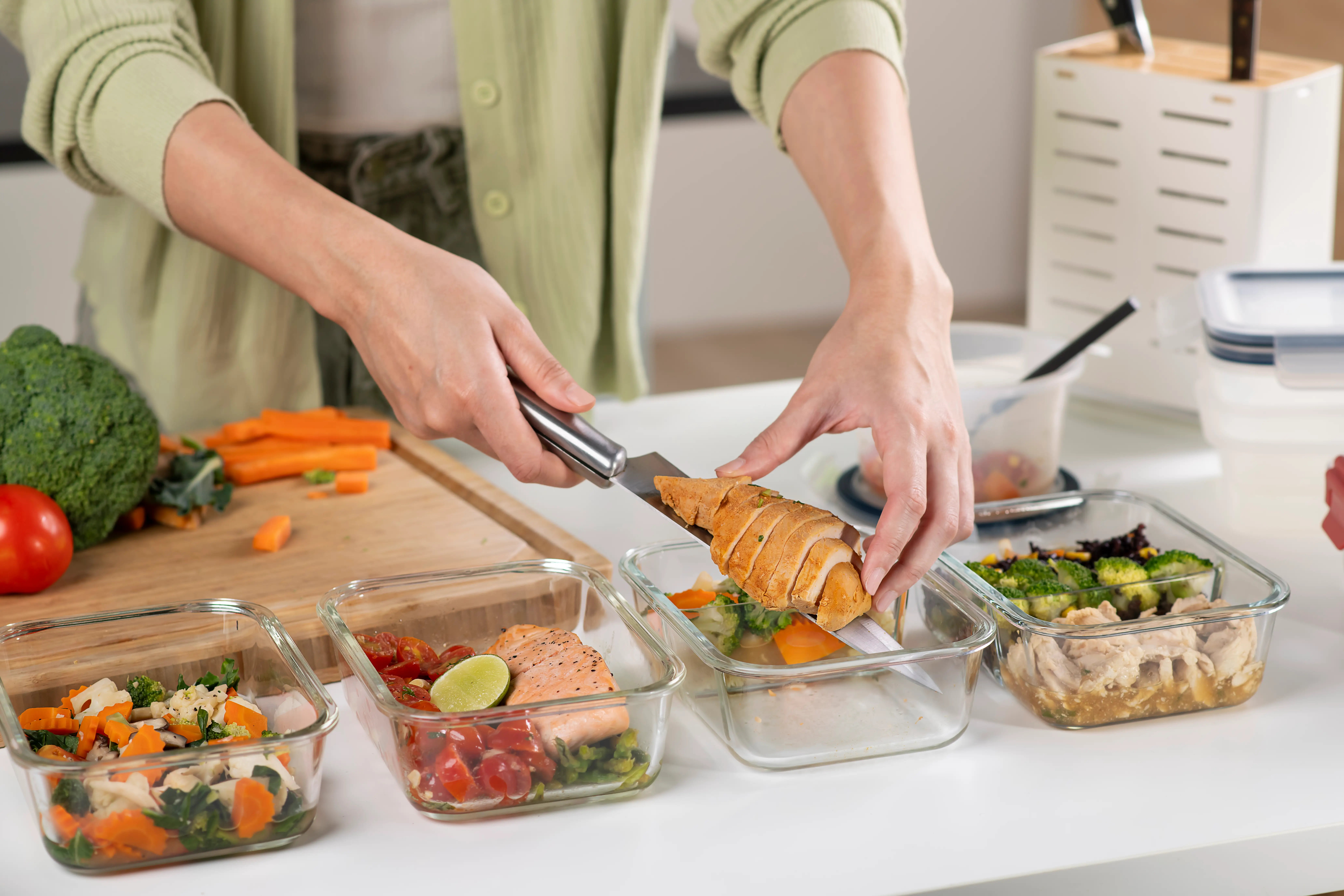 A close up of a woman meal prepping chicken and vegetables.