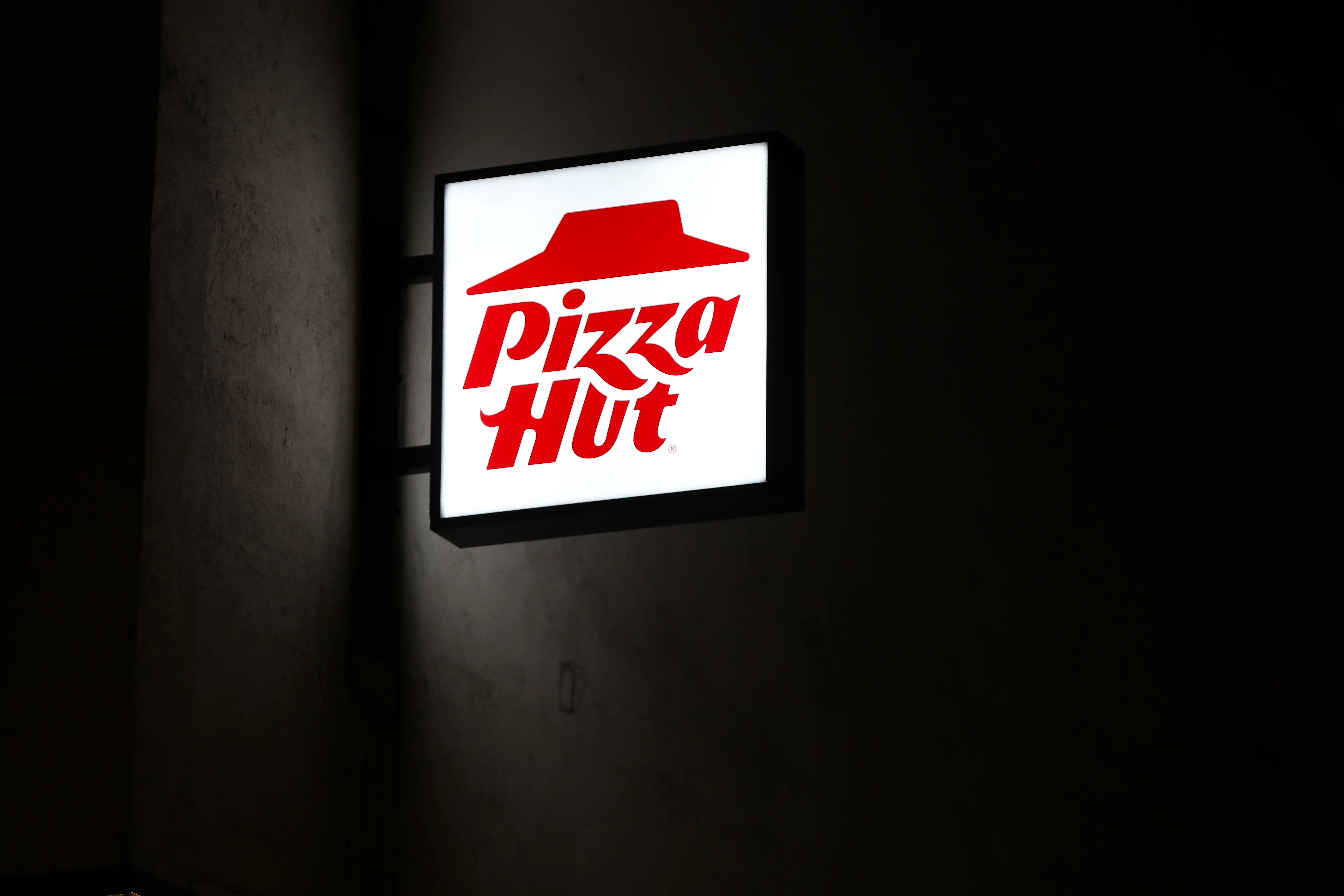An illuminated Pizza Hut sign on the side of a building at night.