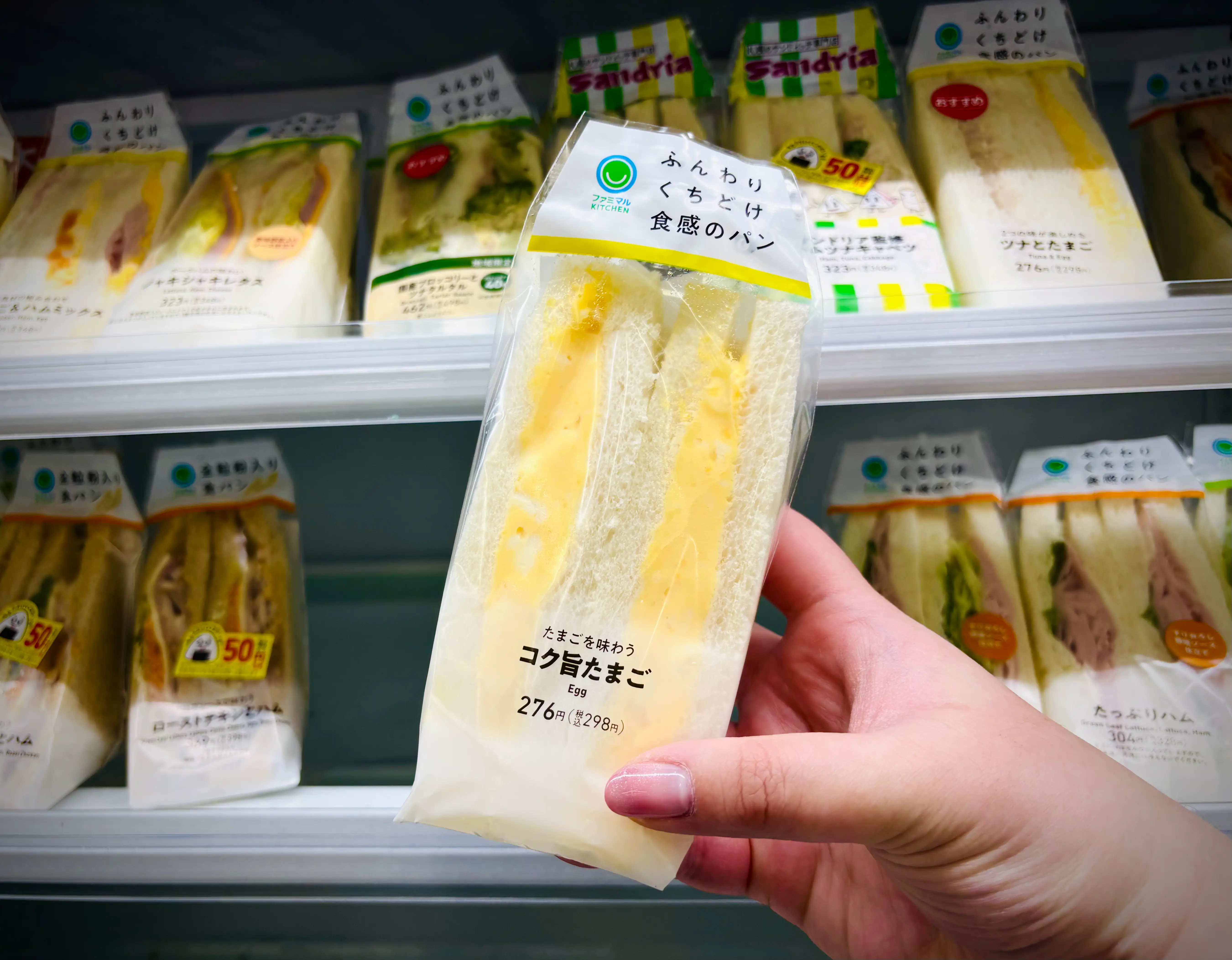 Hand holds a packaged egg sandwich in front of refrigerated convenience store sandwich shelves.