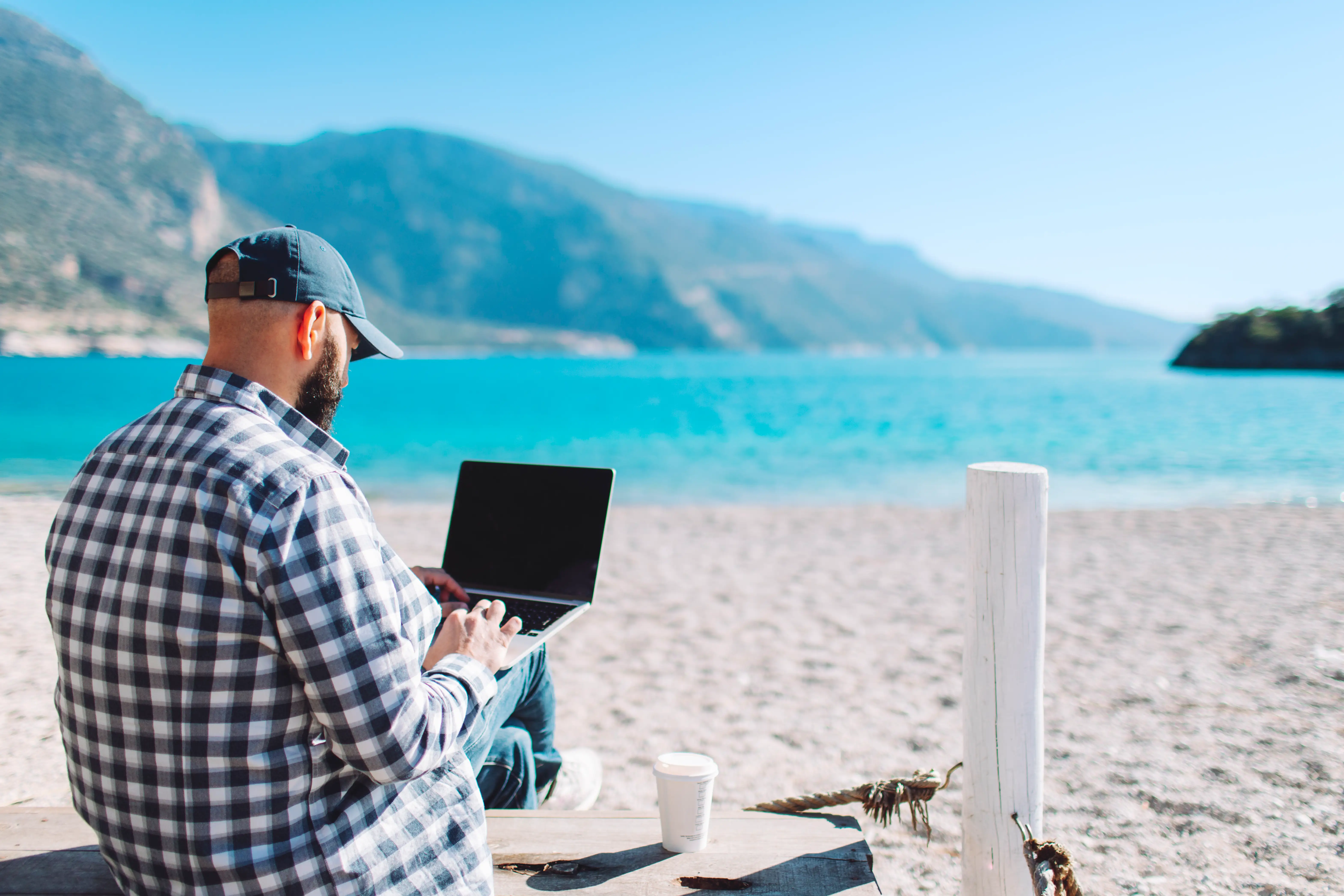 Young adult man working at the beach using laptop