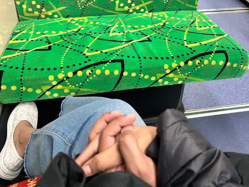 The writer and her partner holding hands on a train in Melbourne, with a green seat nearby.