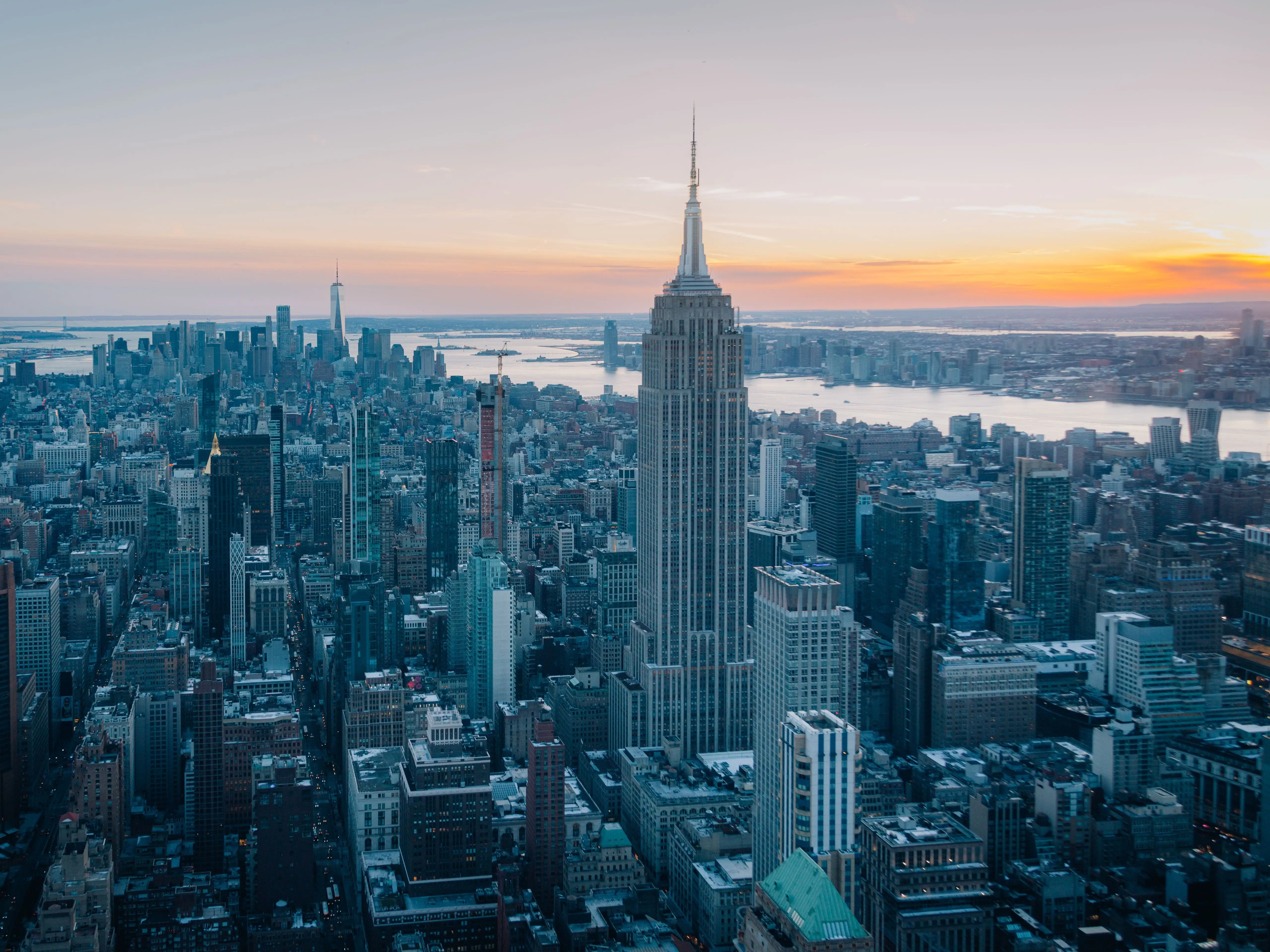 Aerial view of the New York City skyline at sunset featuring the Empire State Building and surrounding skyscrapers.