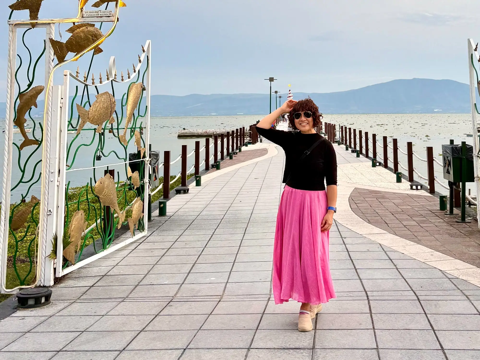 Woman smiling with hand on hair on walkway by water