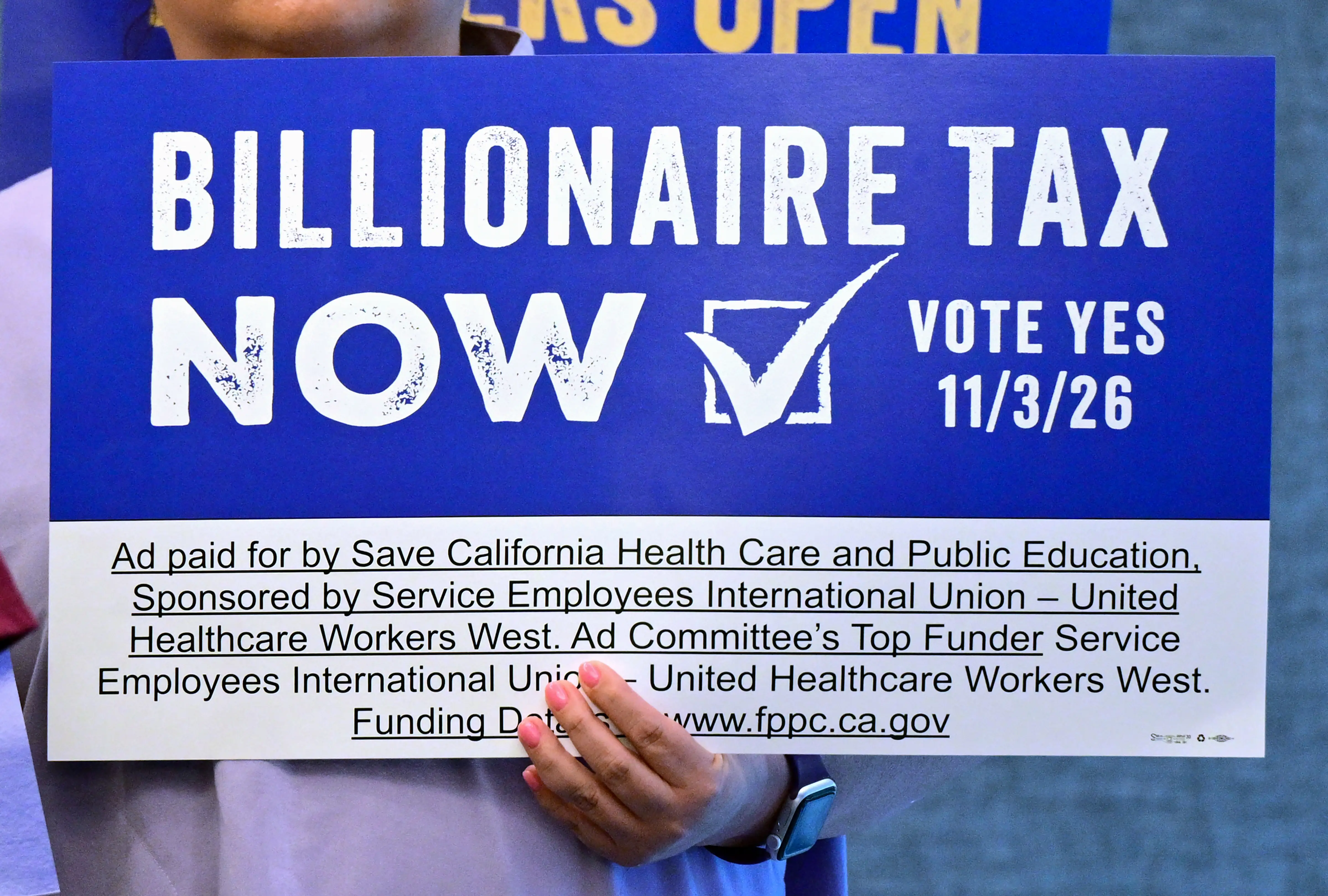 A supporters with the Billionaire Tax Now coalition hold a placard during a media briefing in Los Angeles on April 27, 2026.