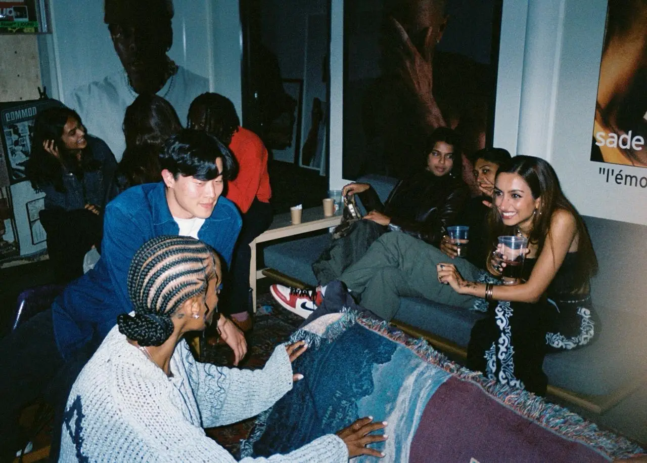Film camera photo of five people sitting around drinking wine on a sofa.