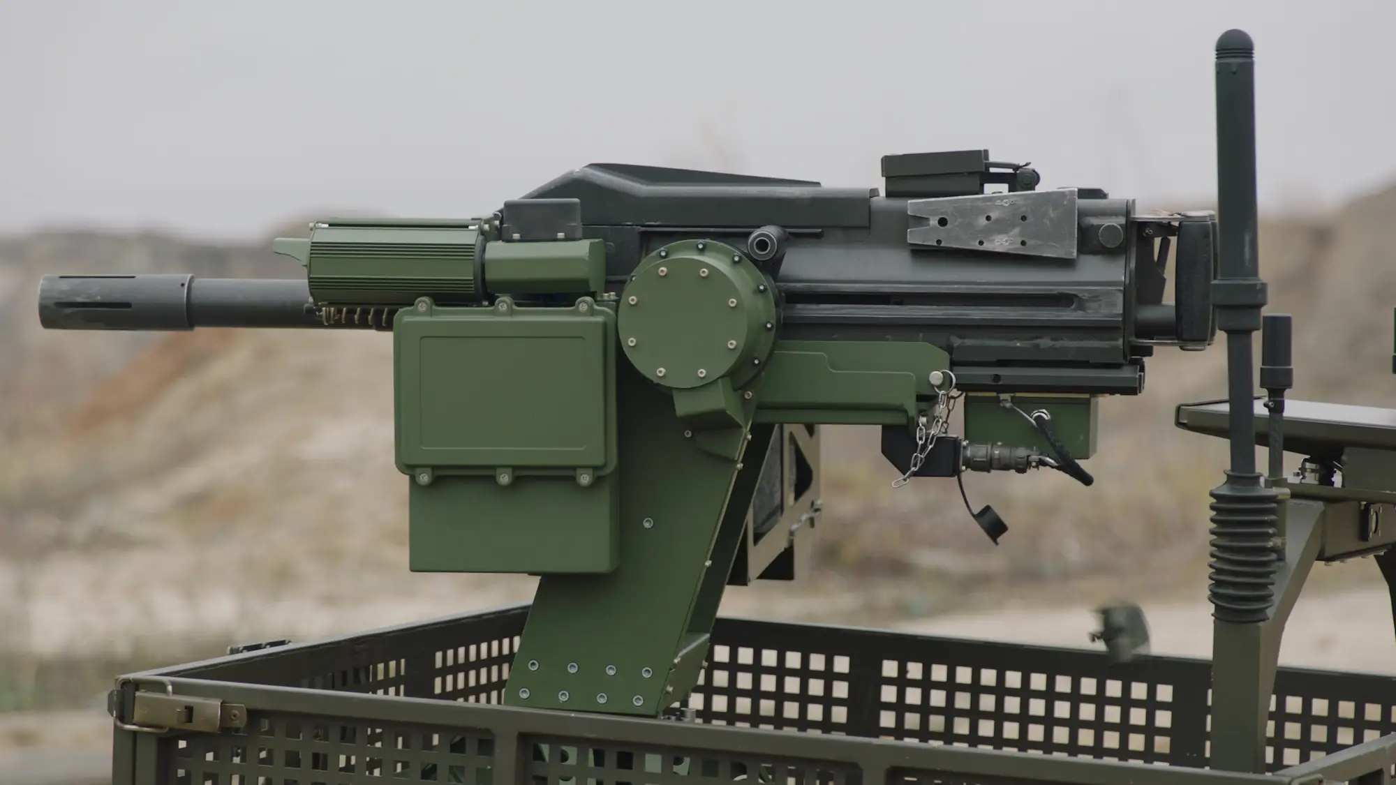 A green mounted heavy weapon system on a vehicle platform in an outdoor area.