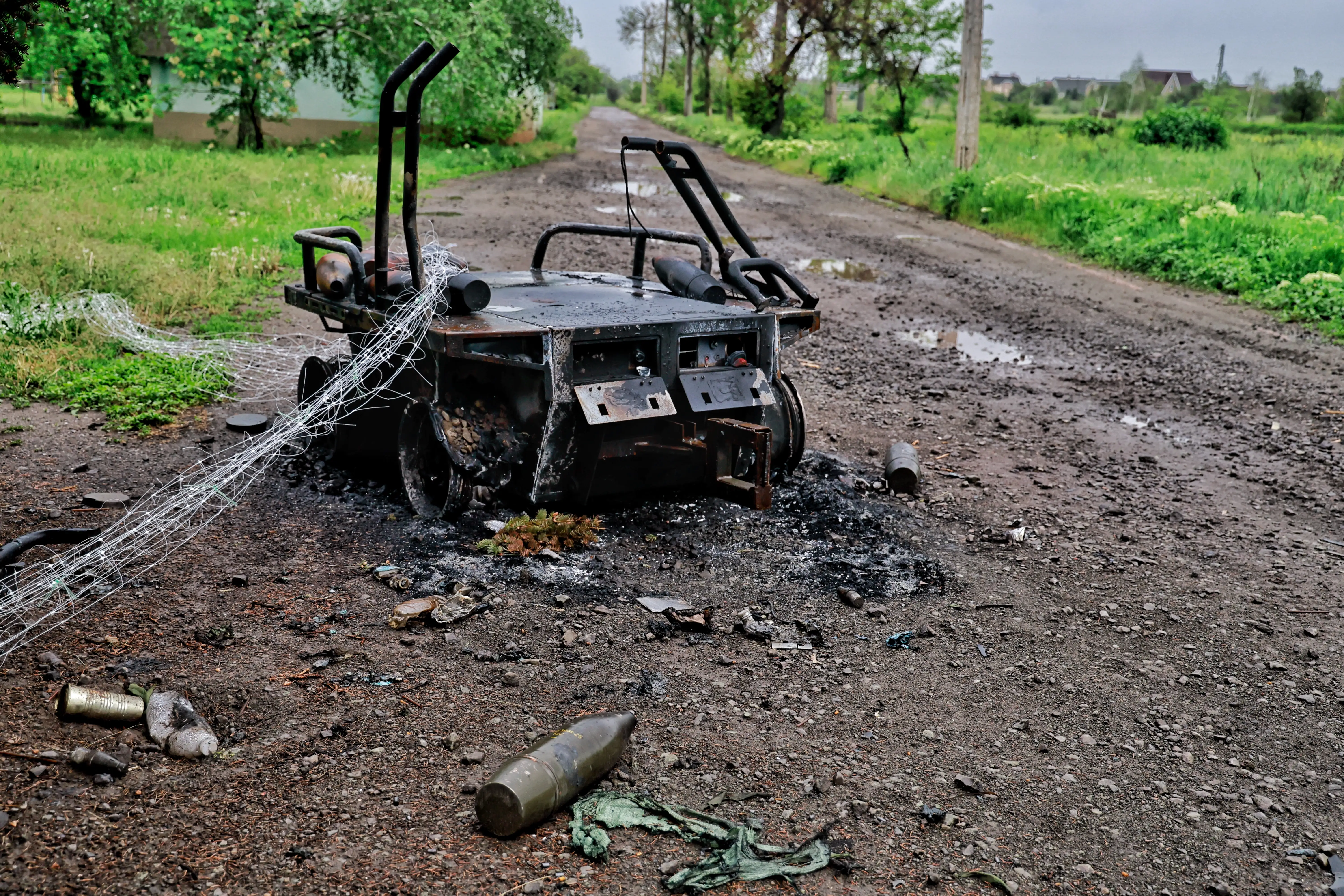 A broken and burnt robot on a dirt road with green grass on either side