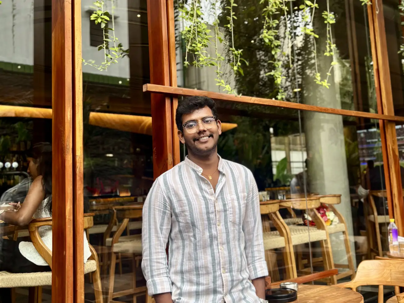 Rathesh Prabakar is wearing a button-up shirt and standing outside a restaurant.