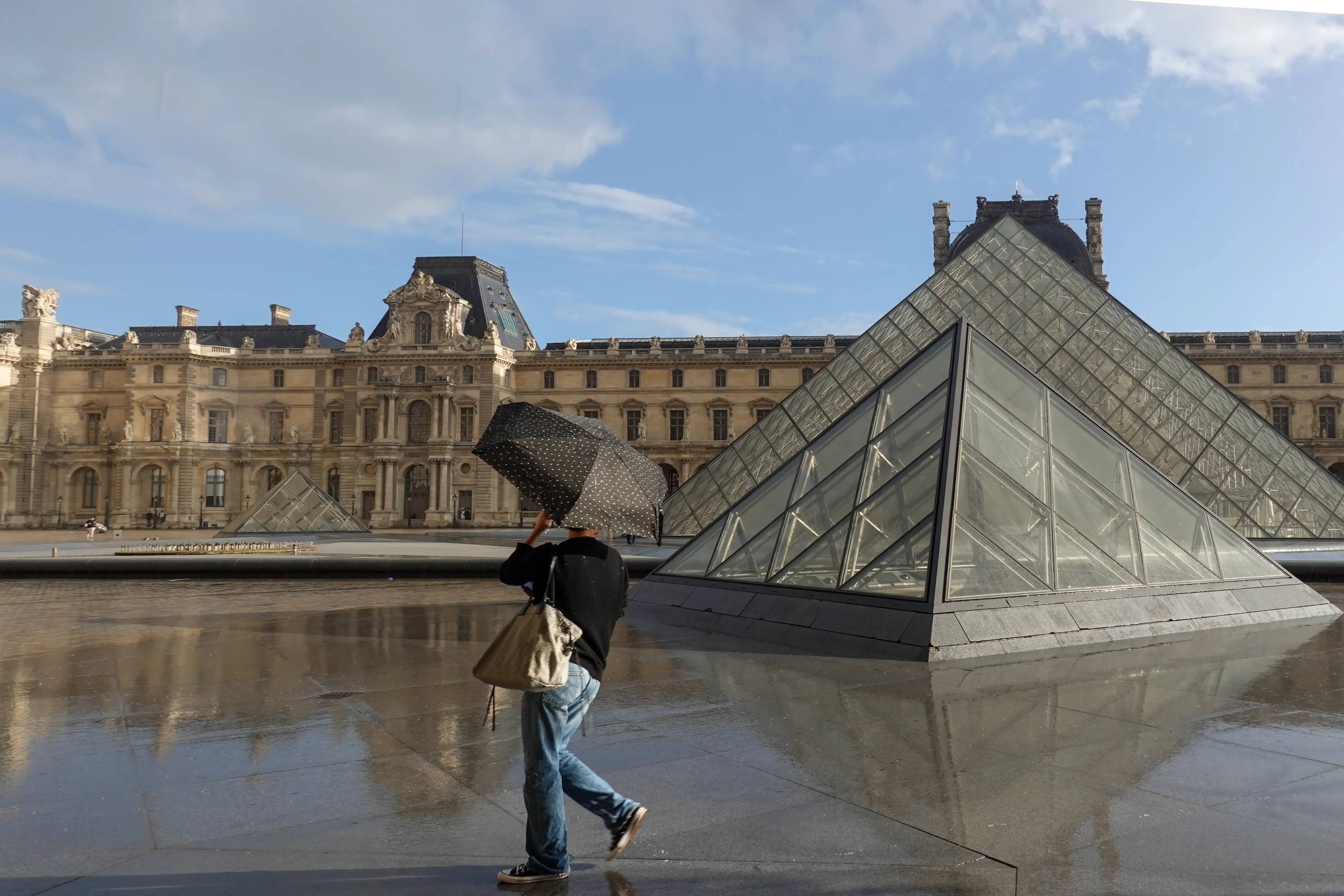 View of Louvre in paris in the rain, person walking past with umbrella