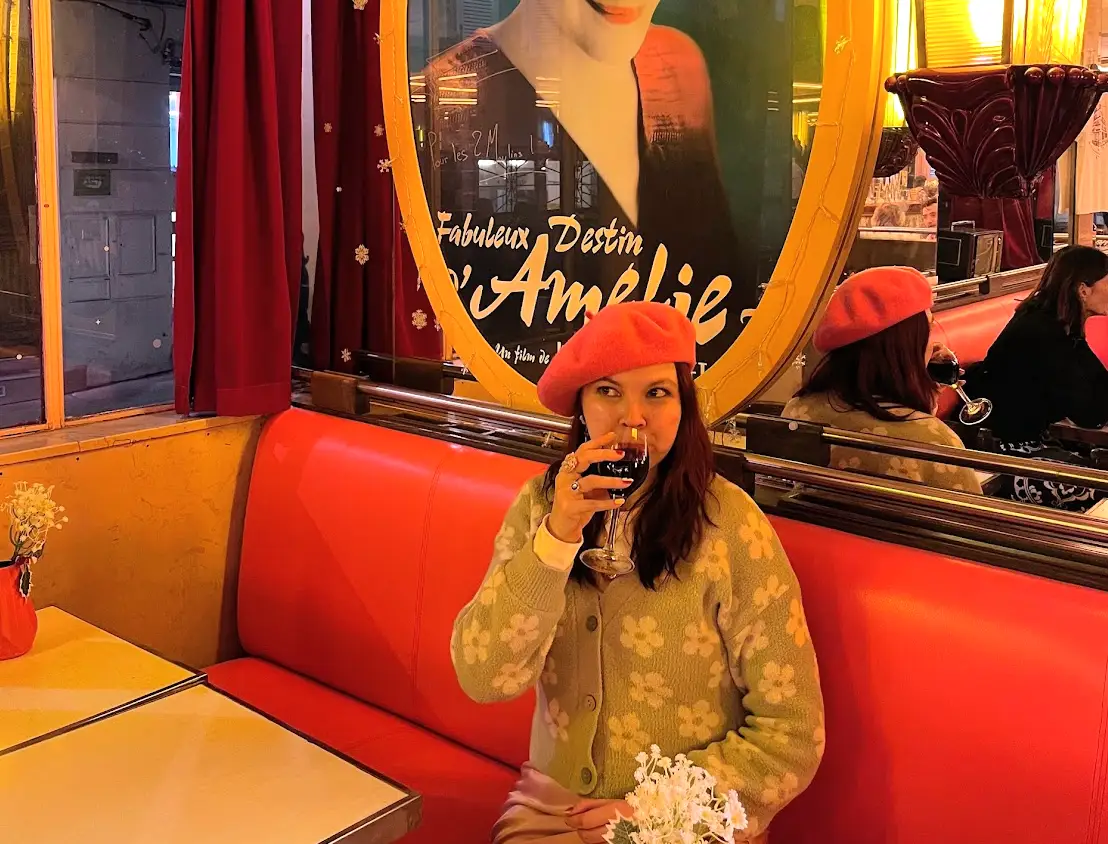 The writer sitting in a red booth, drinking a glass of wine in front of an Amelie sign in Paris.