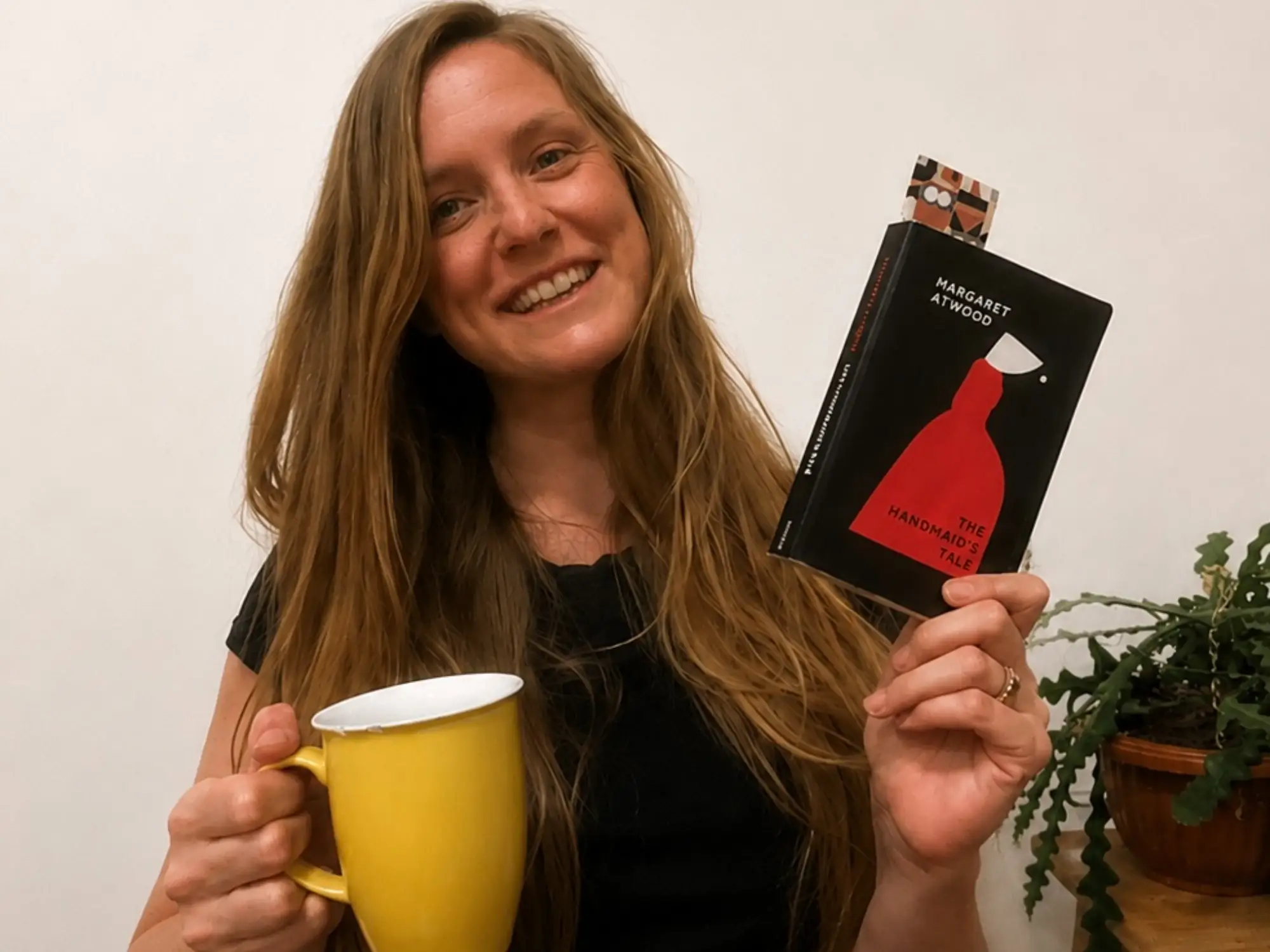 Woman smiling holding copy of the handmaid's tale book and a coffee mug