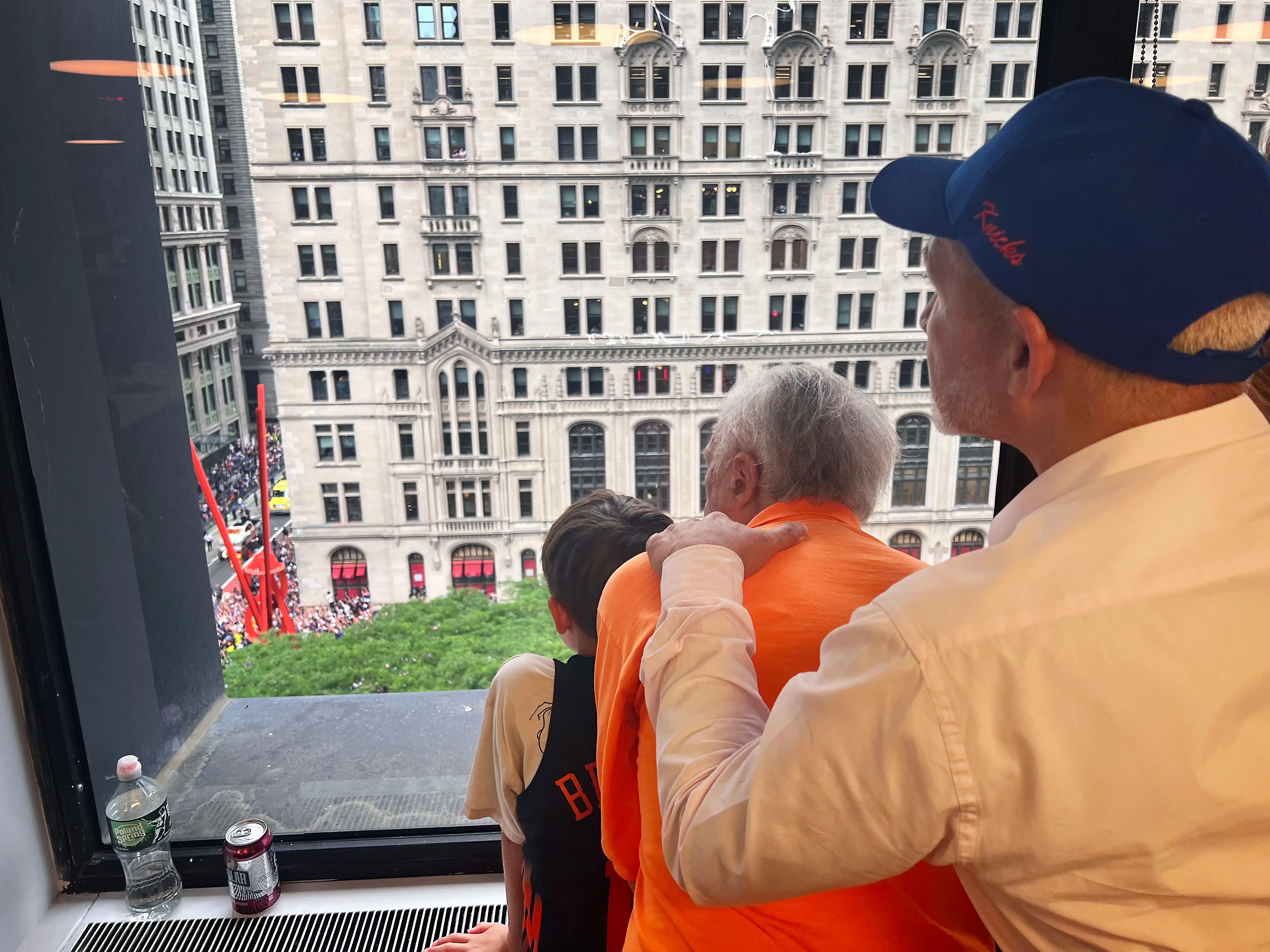 Three people look out of a high window at a crowded city street for the Knicks parade.