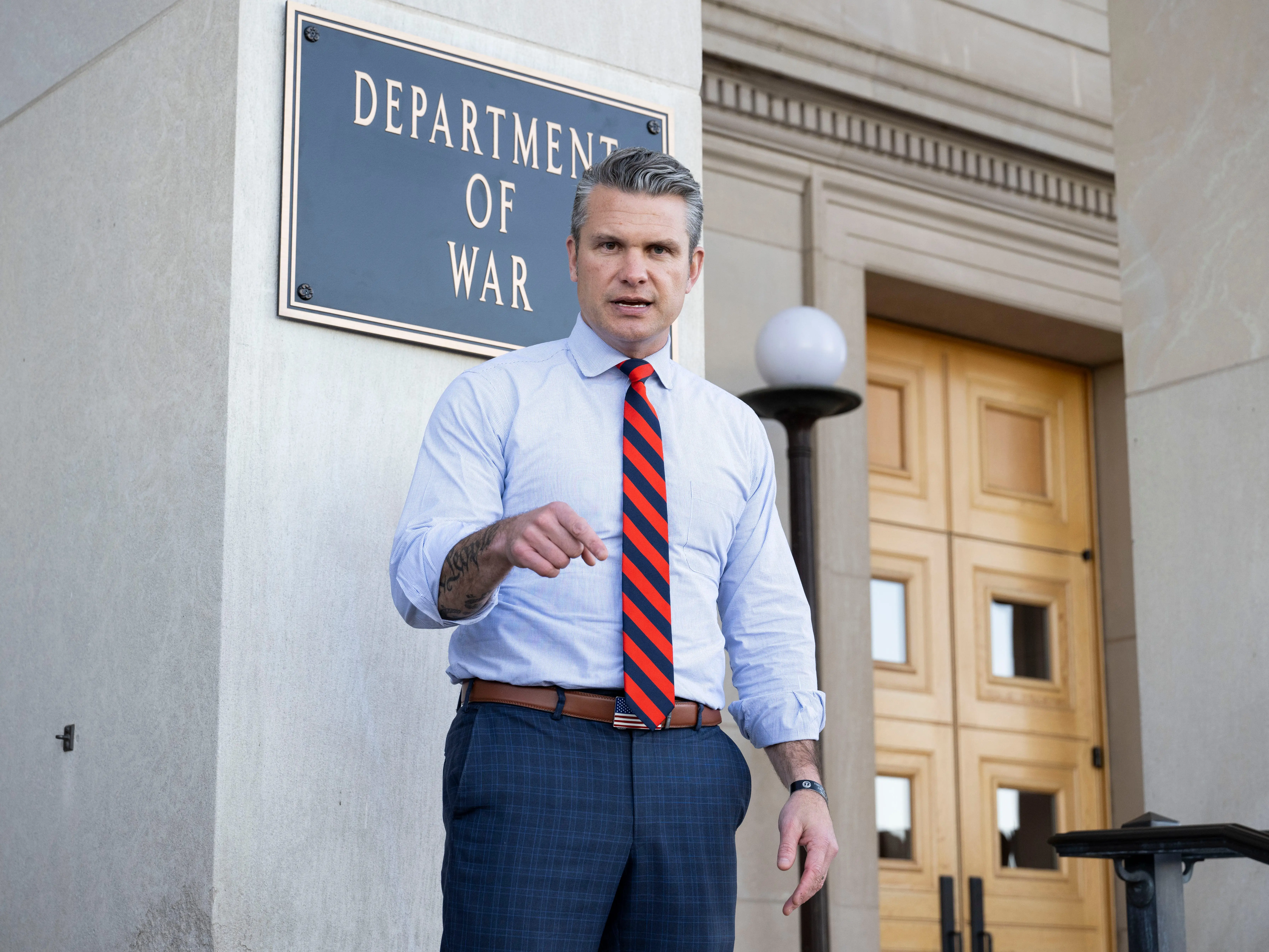 Secretary of Defense Pete Hegseth standing in front of a Department of War sign