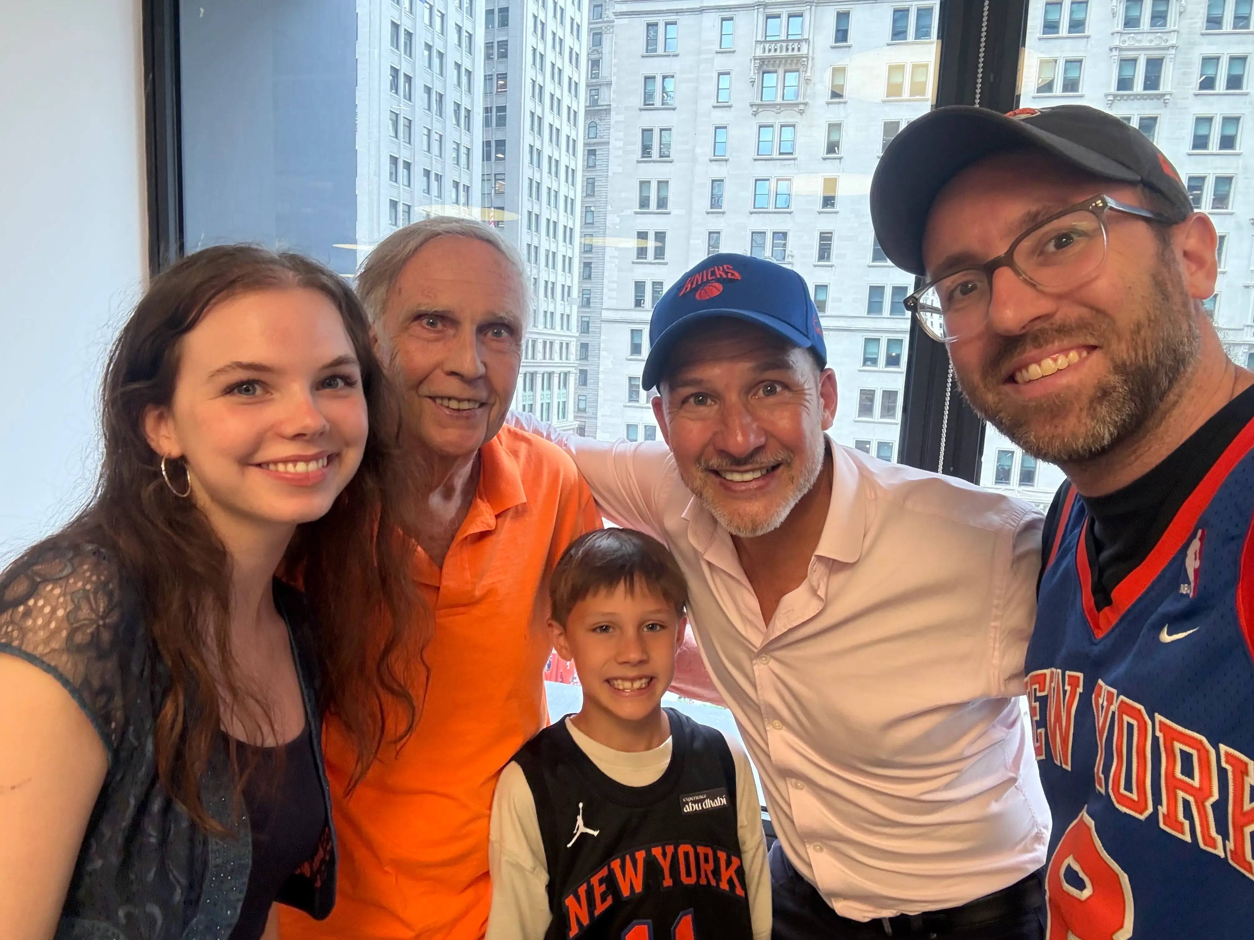 Five people smile for a group photo by office windows overlooking New York City buildings.