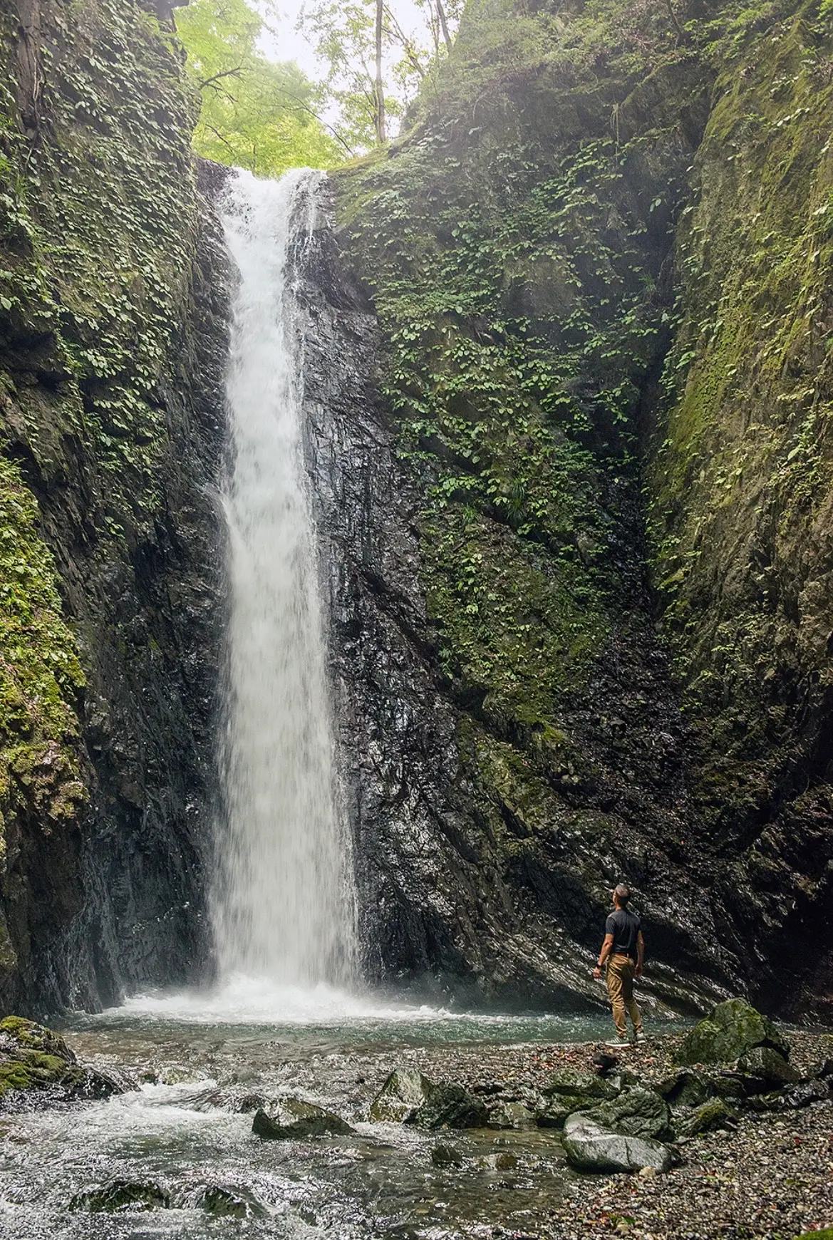A man and the base of a waterfall in rural Japan.