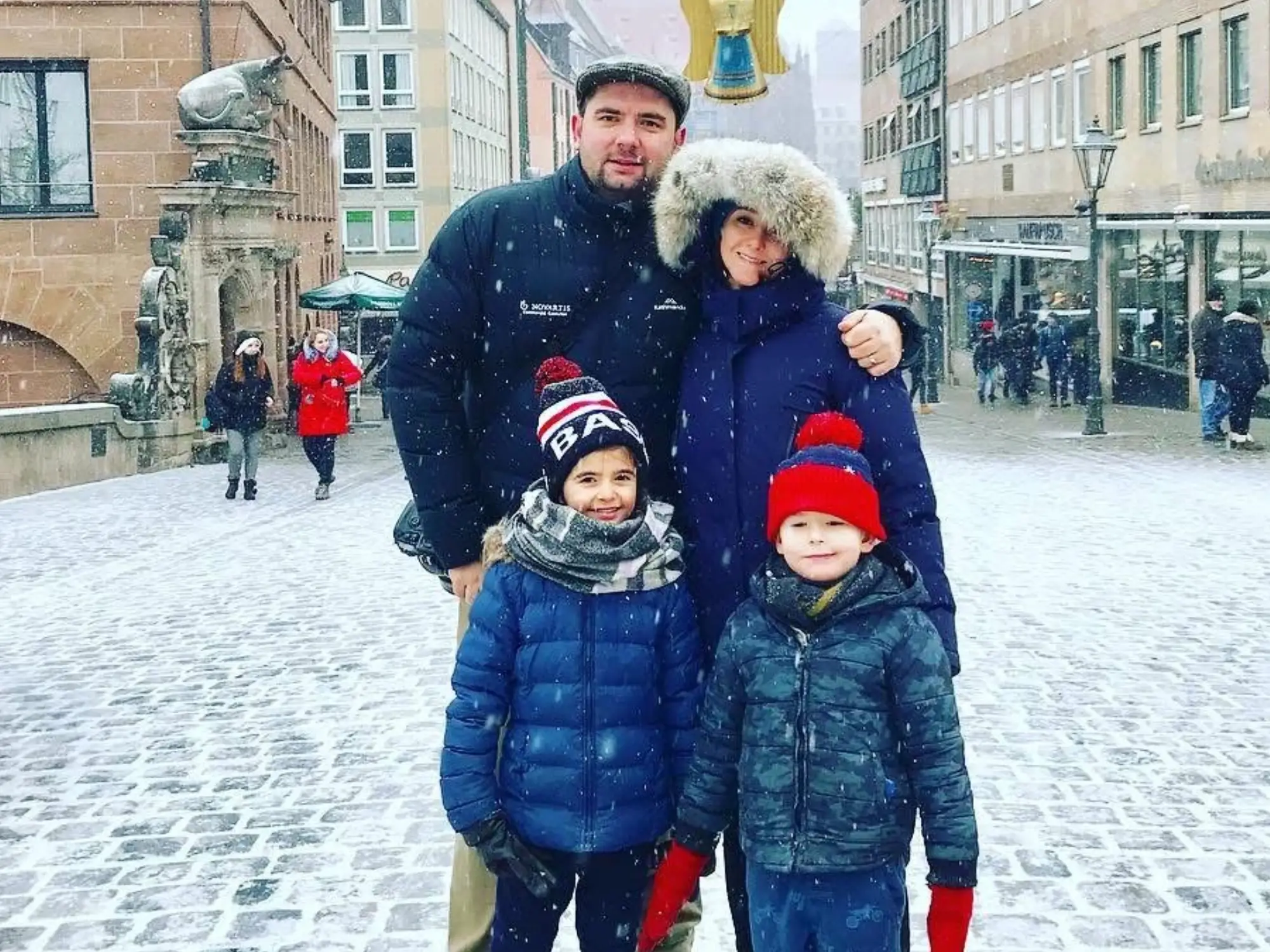 Man, woman and two kids smiling at Christkindlesmarkt in Europe in snow