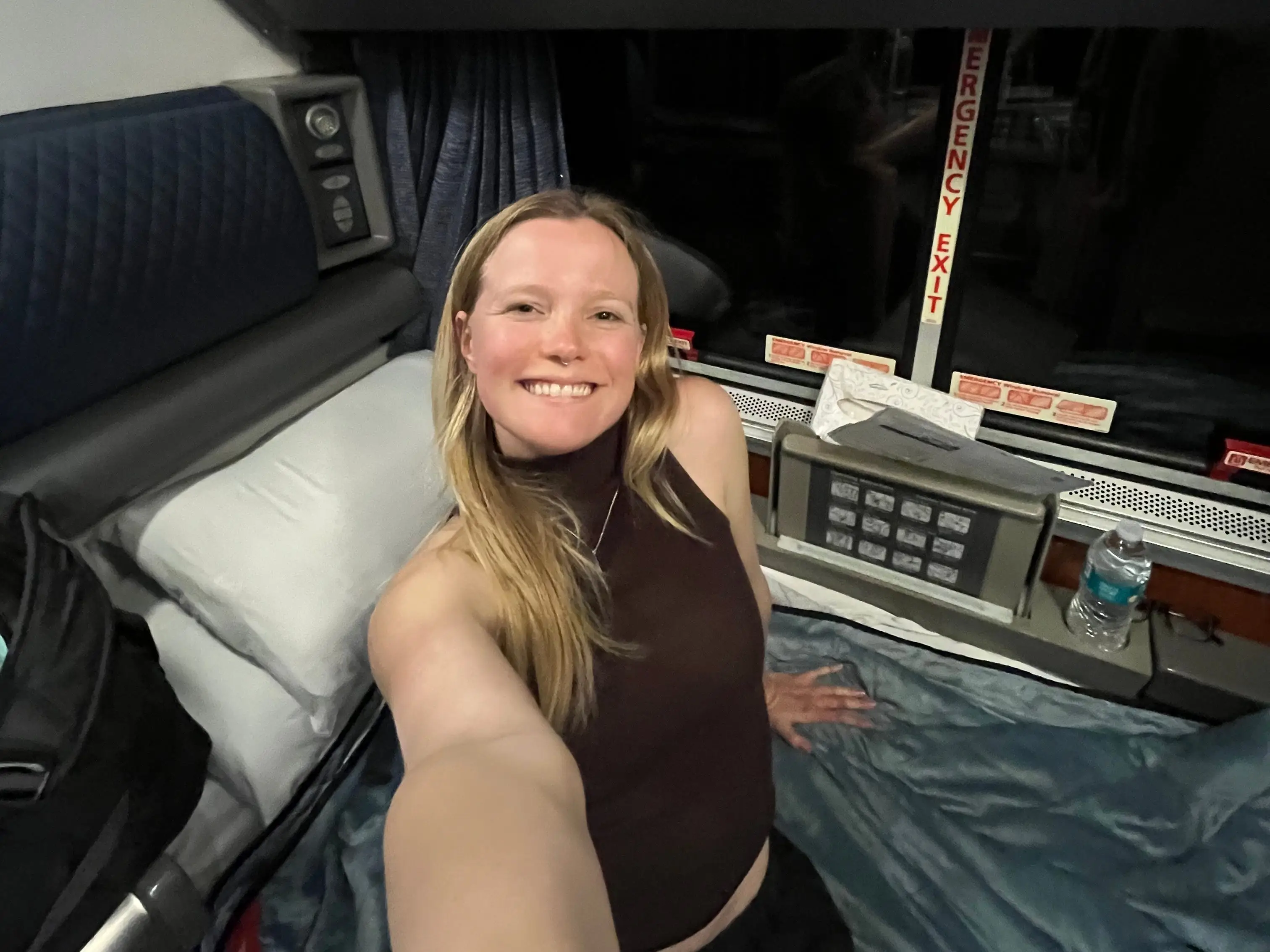 A woman sitting on a bed in an Amtrak roomette.