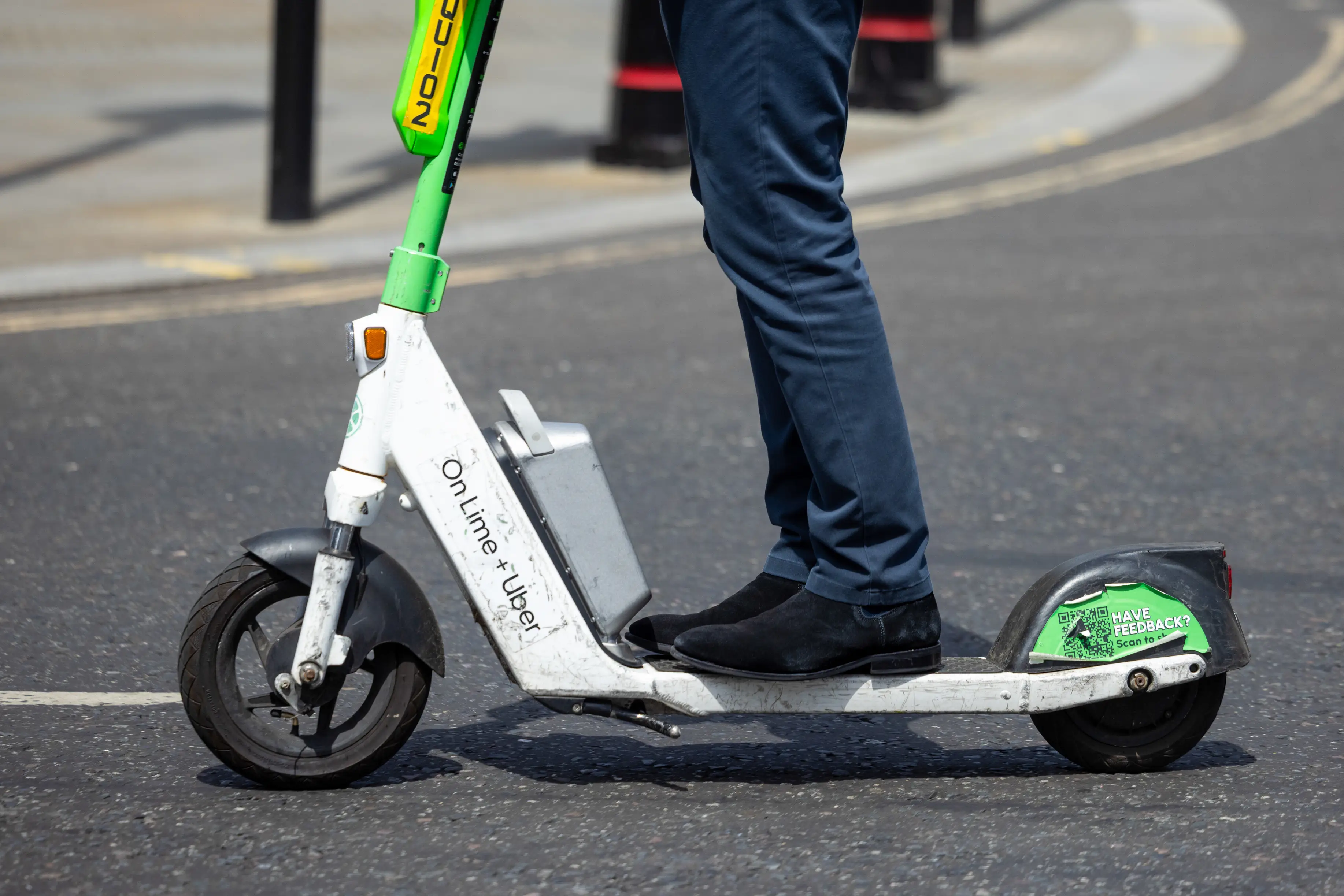 A person rides a Lime electric scooter, with only their black boots and blue pants visible in the photo.