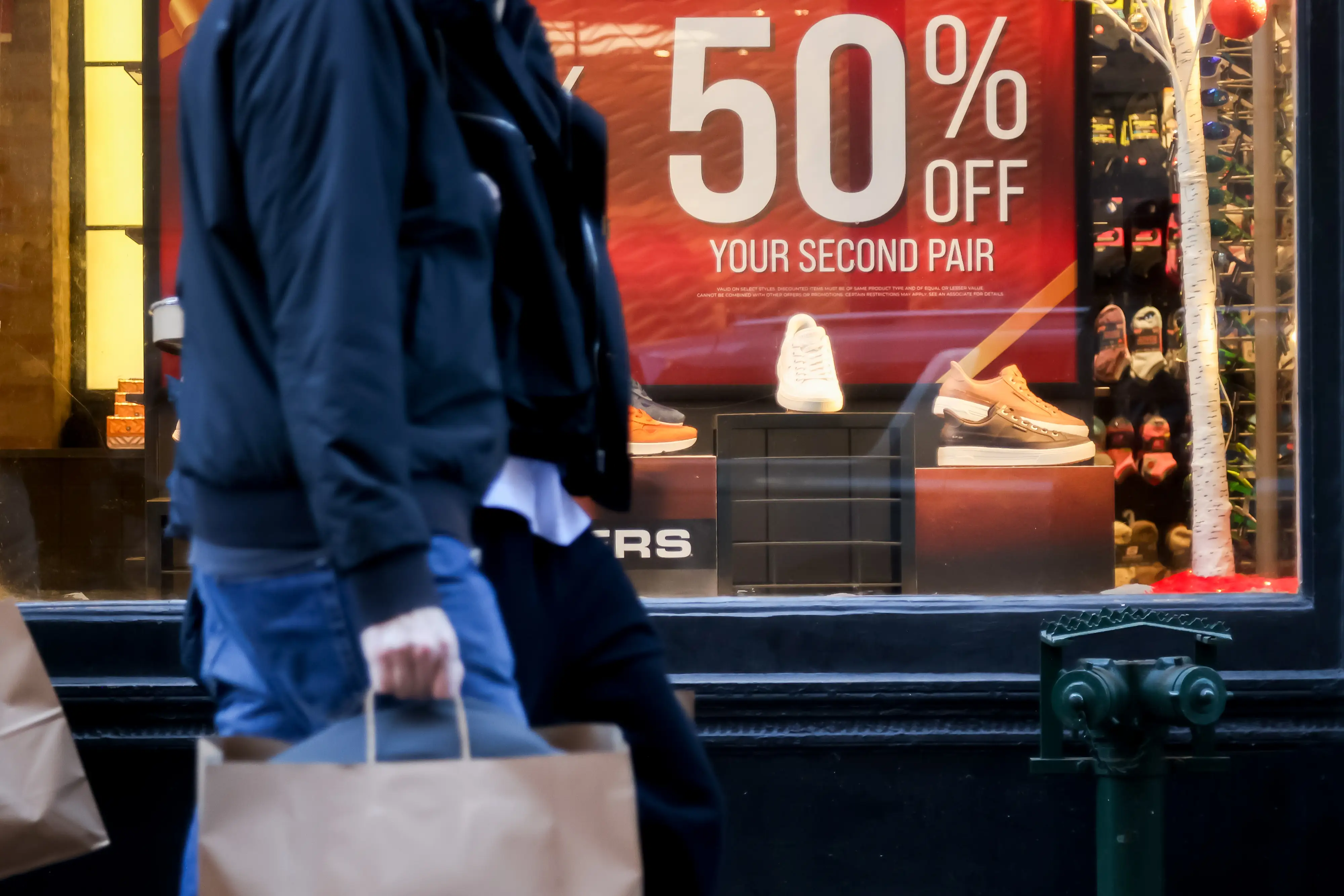 People walking down the street next to a sale window.