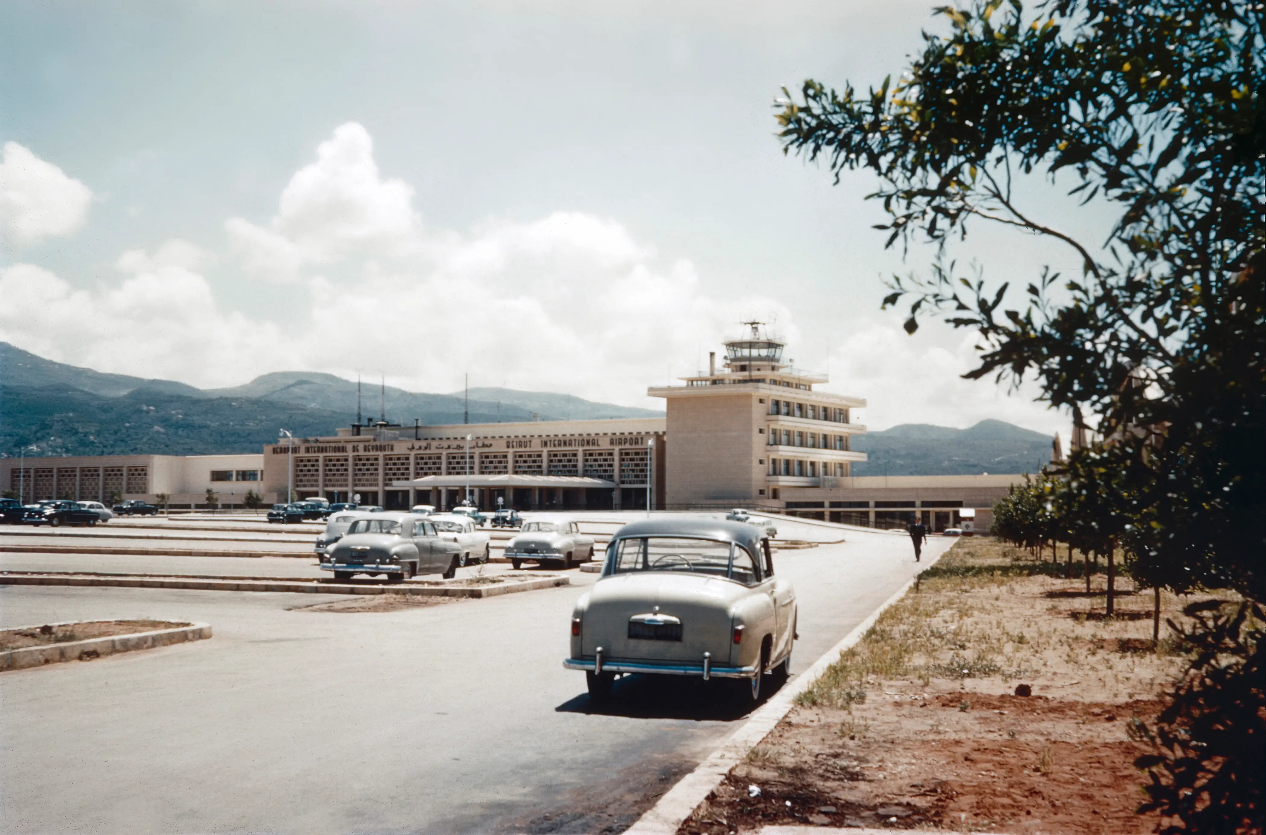 Historic color photograph (digitized slide) taken in 1966, showing a view from the parking area toward Beirut International Airport in Lebanon. The image captures the mid-20th-century architecture and atmosphere of air travel during that era,