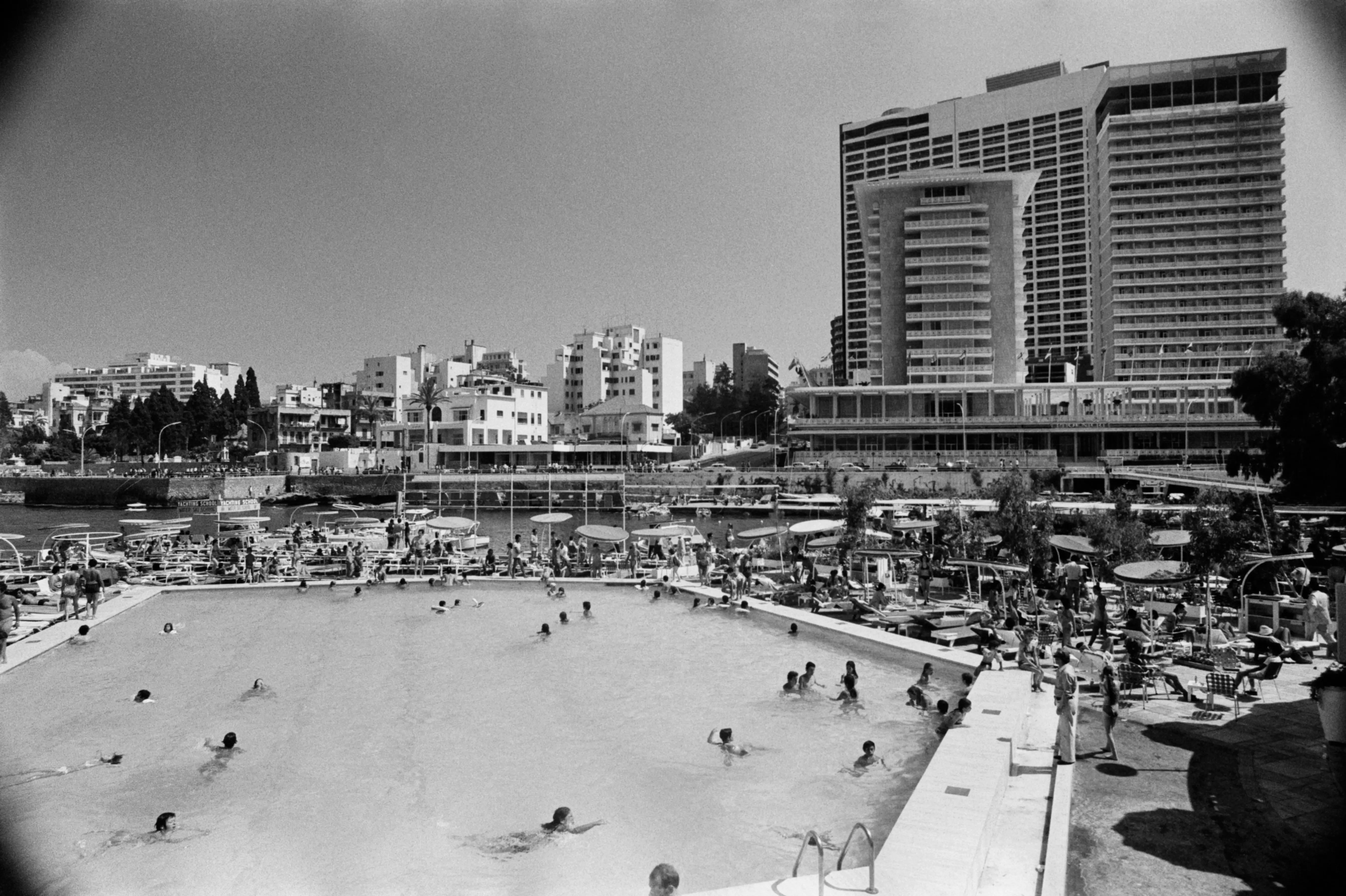 Guests fill the swimming pool and garden of the St. Georges Beach Club. The Phoenicia Intercontinental Hotel rises in the background.