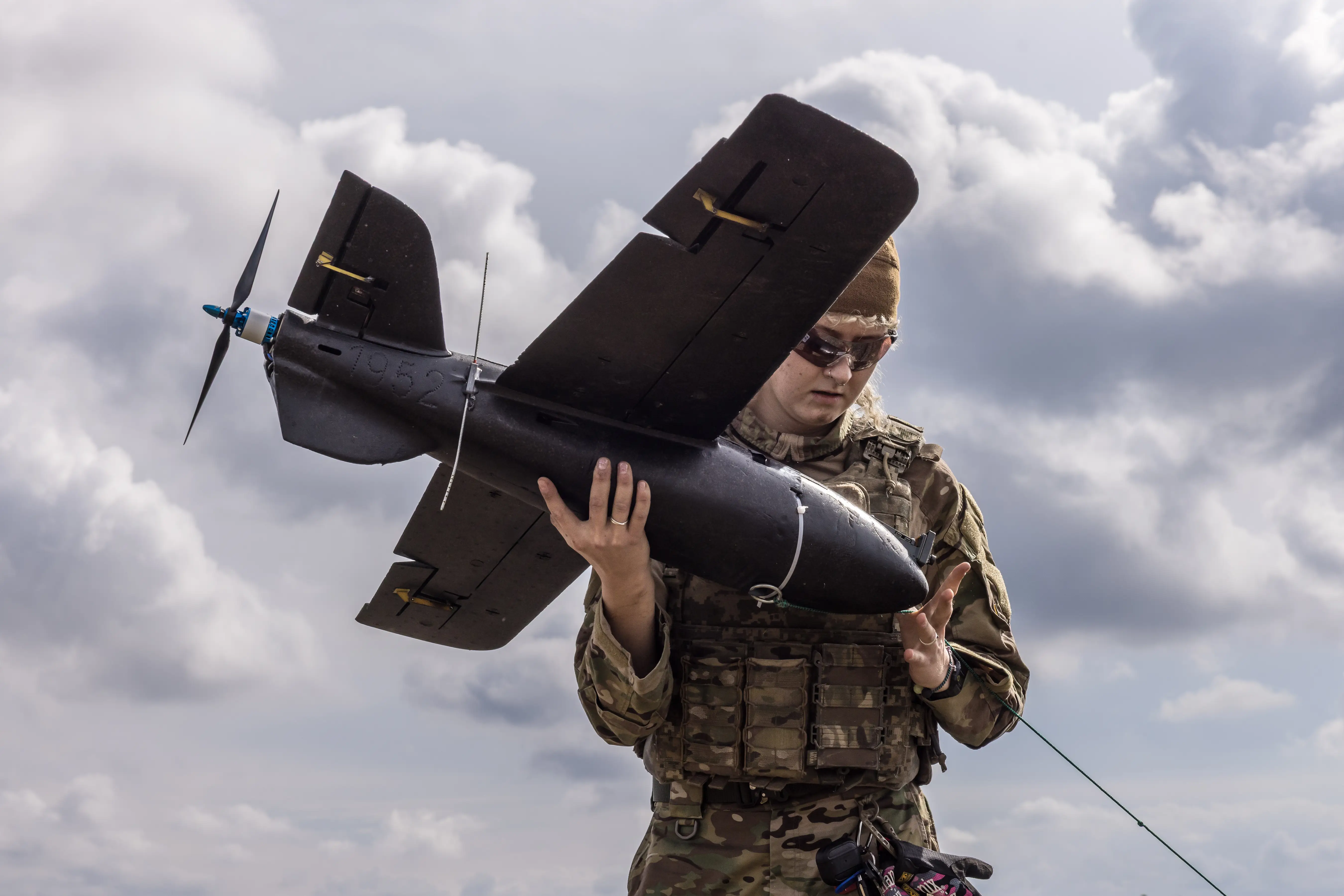 A female Ukrainian soldier holds a drone in her right hand while her left attaches it to a launch system.
