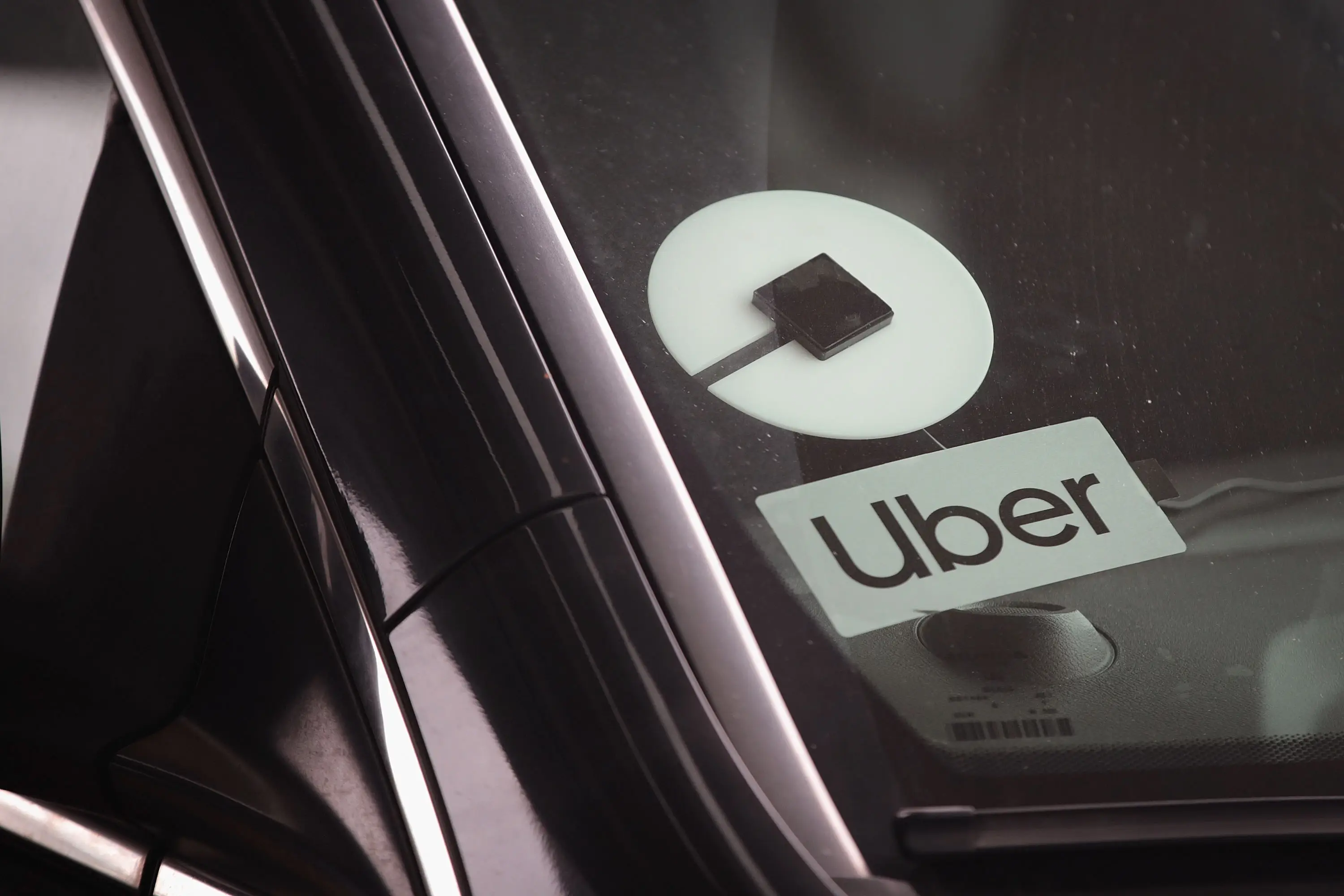 An Uber logo sticker is seen in the windshield of a black car.