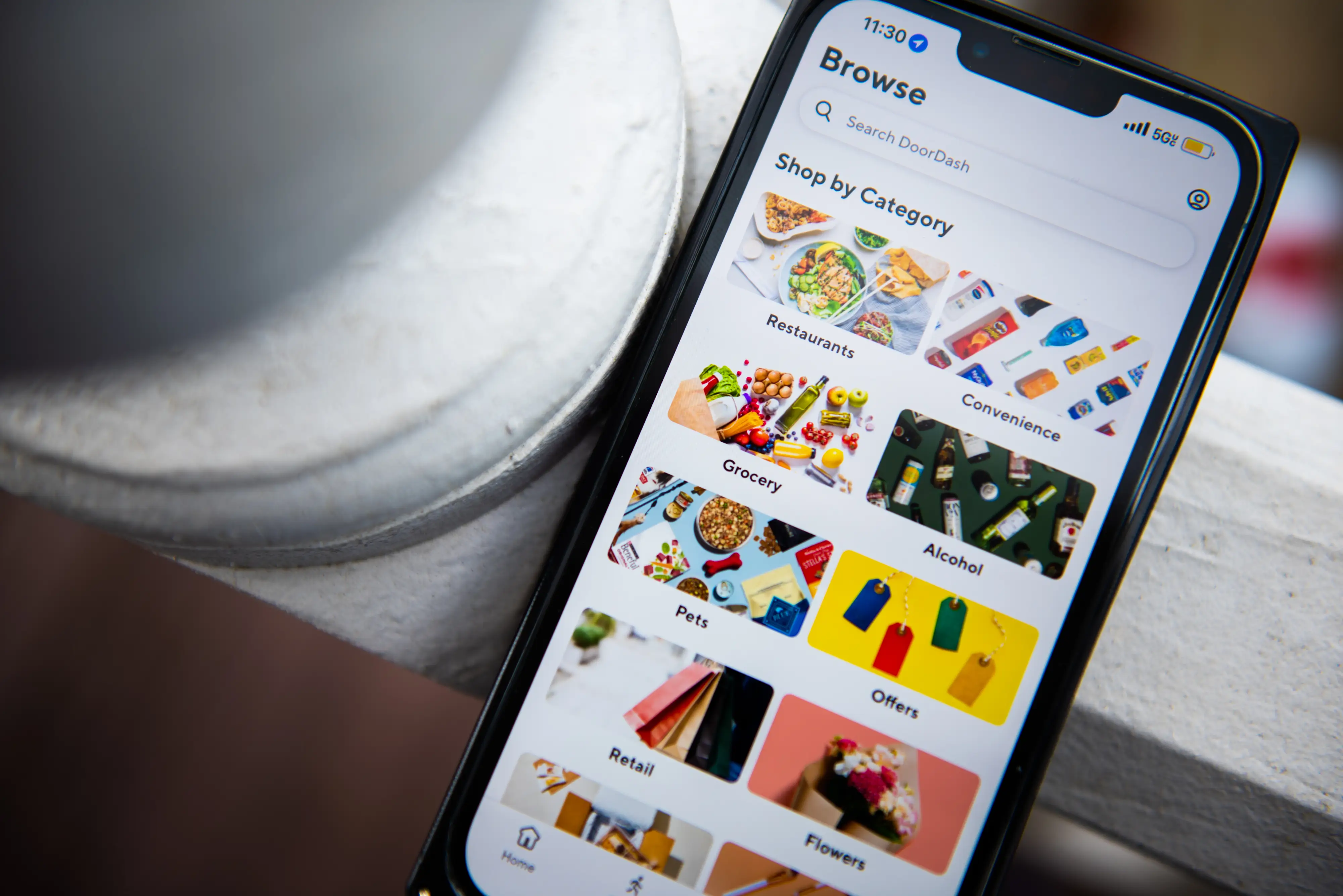 An iPhone shows the DoorDash app, including categories of items such as grocery and restaurants.