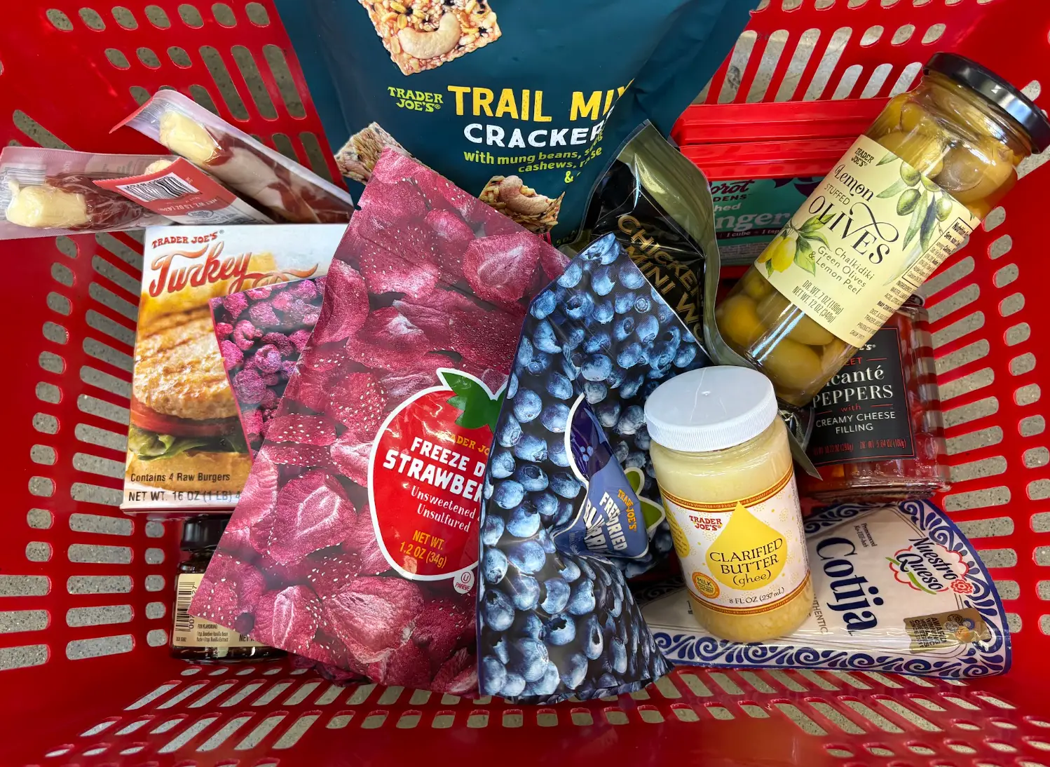 A red cart full of Trader Joe's products, including freeze-dried berries, lemon-stuffed olives, ghee, and trail-mix crackers.