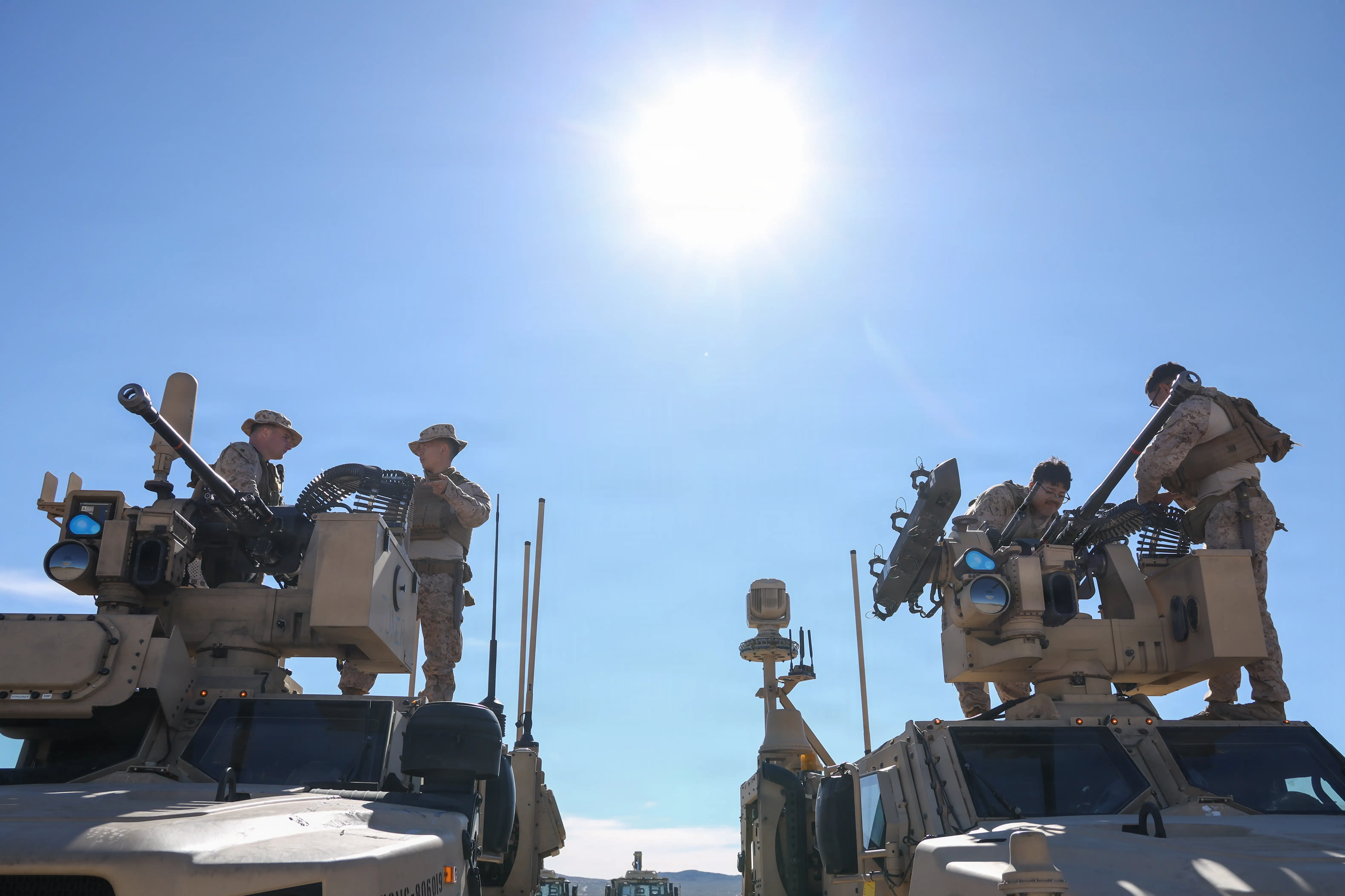 Two vehicles are parked. Marines are standing on top of the vehicles working on weapons that are mounted on the vehicles.