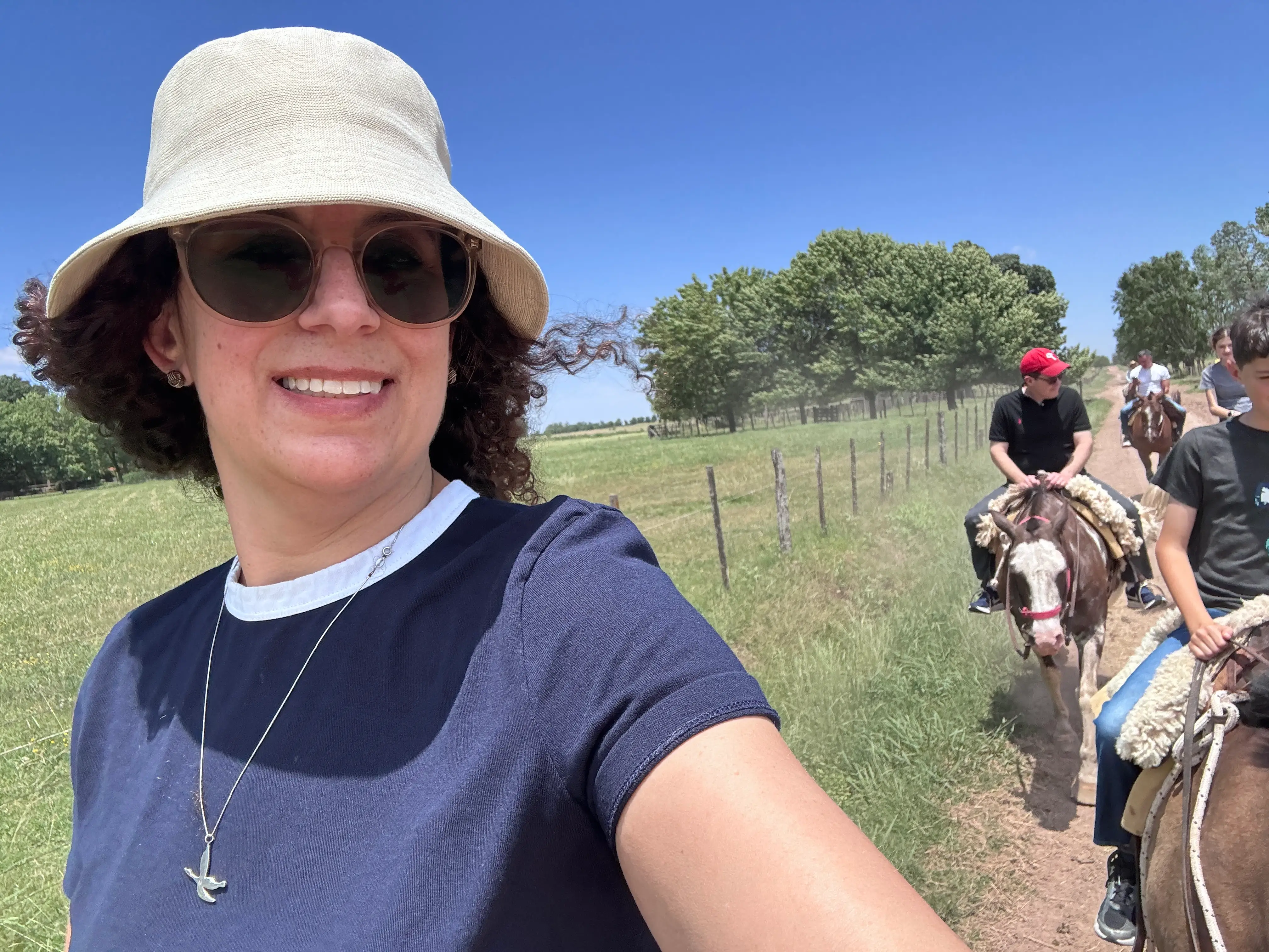 Woman in hat smiling with view of people riding animals behind her