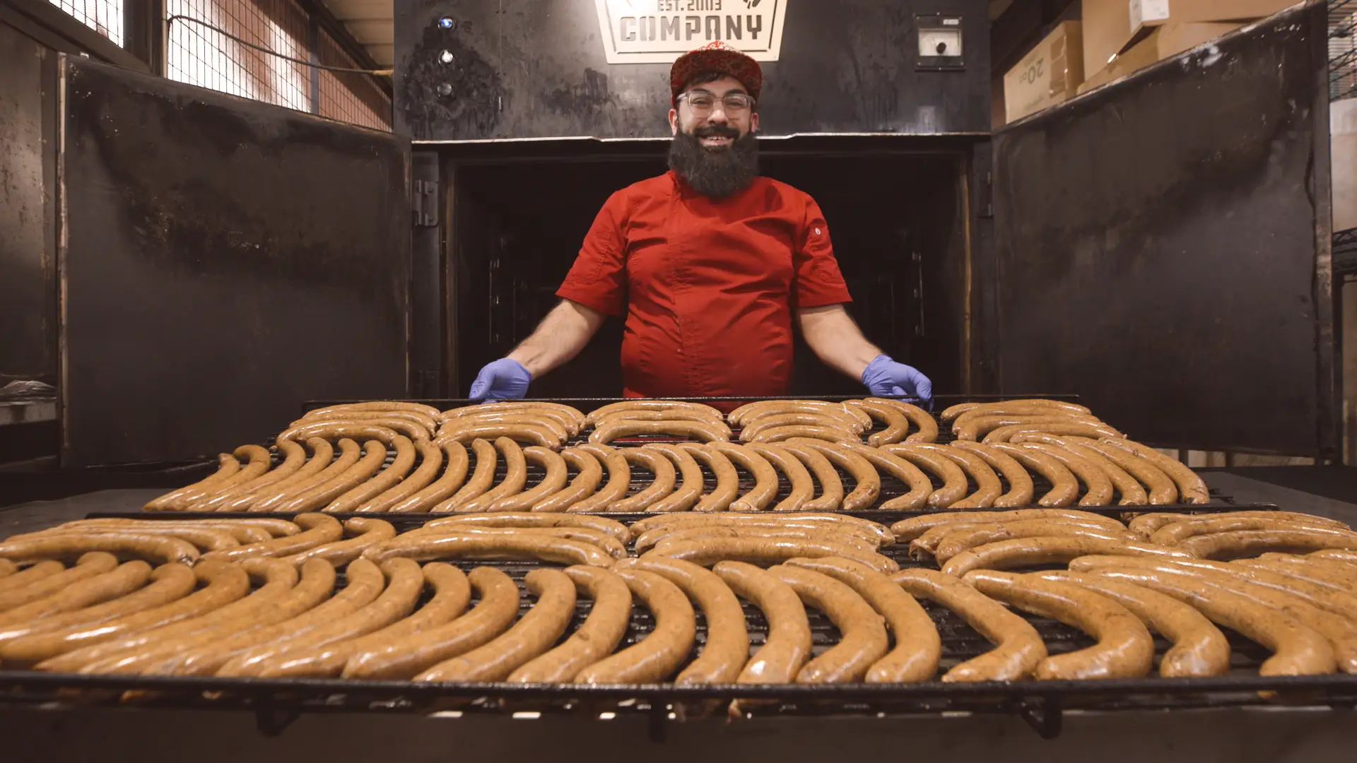 Salahodeen Abdul-Kafi stands in front of dozens of uncooked sausages waiting to be smokes.