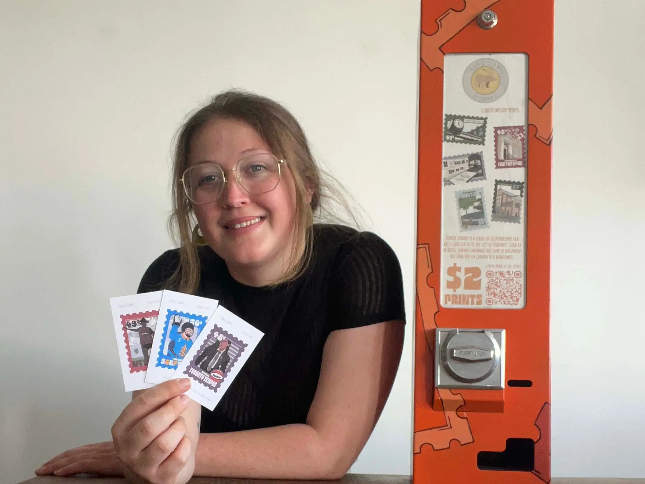 Jemma Chapman holding up her stamp illustrations next to her gum machine