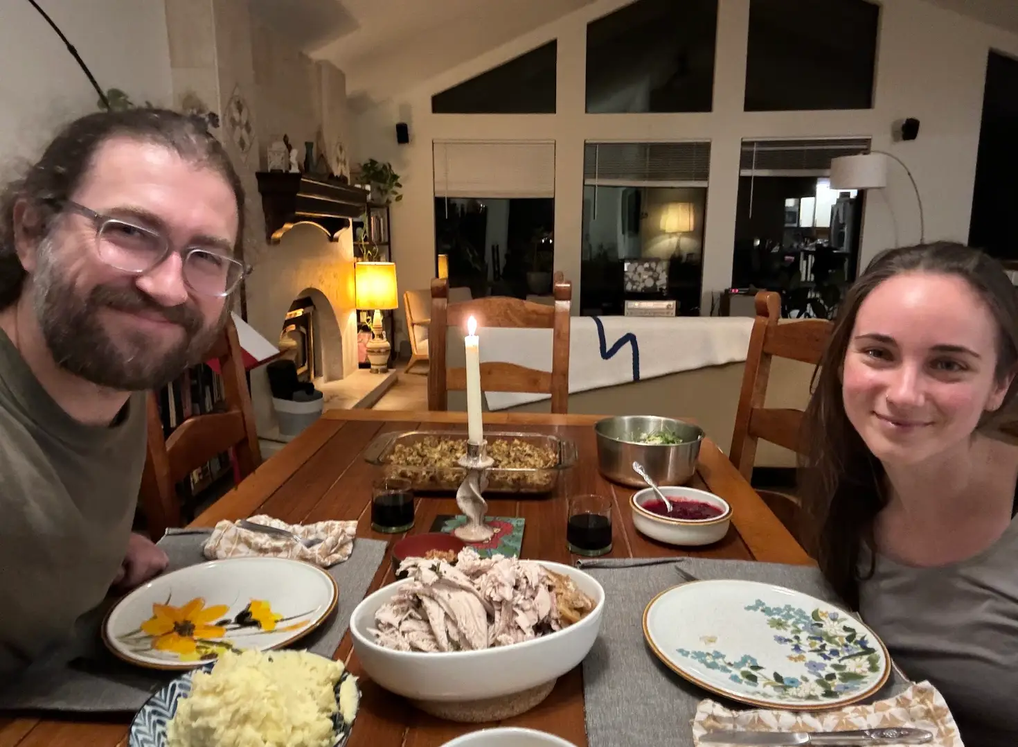 Two people sitting across the table from each other in a house, sharing a candlelit meal.