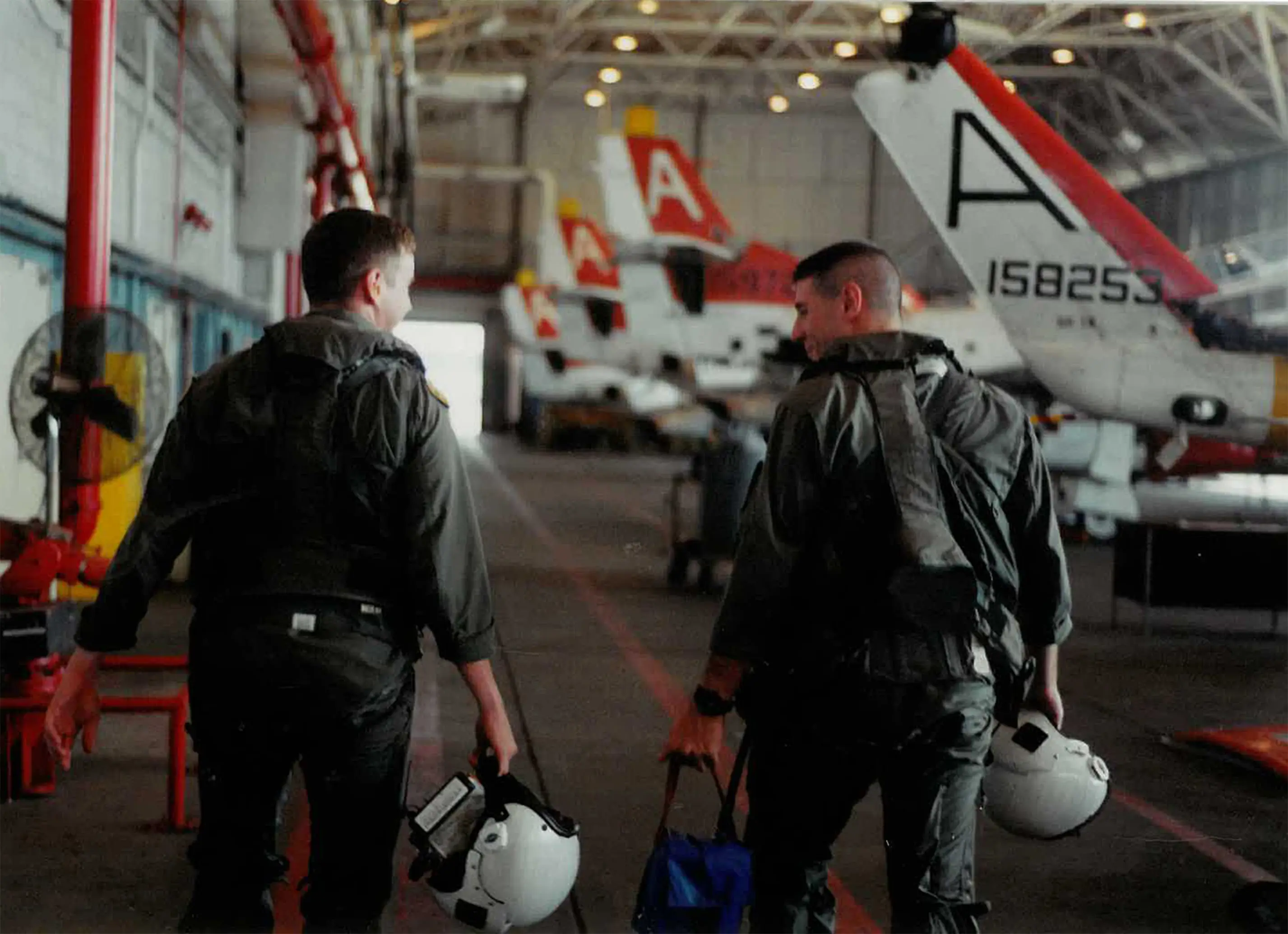 Two fighter pilots walking in a hangar full of jets.