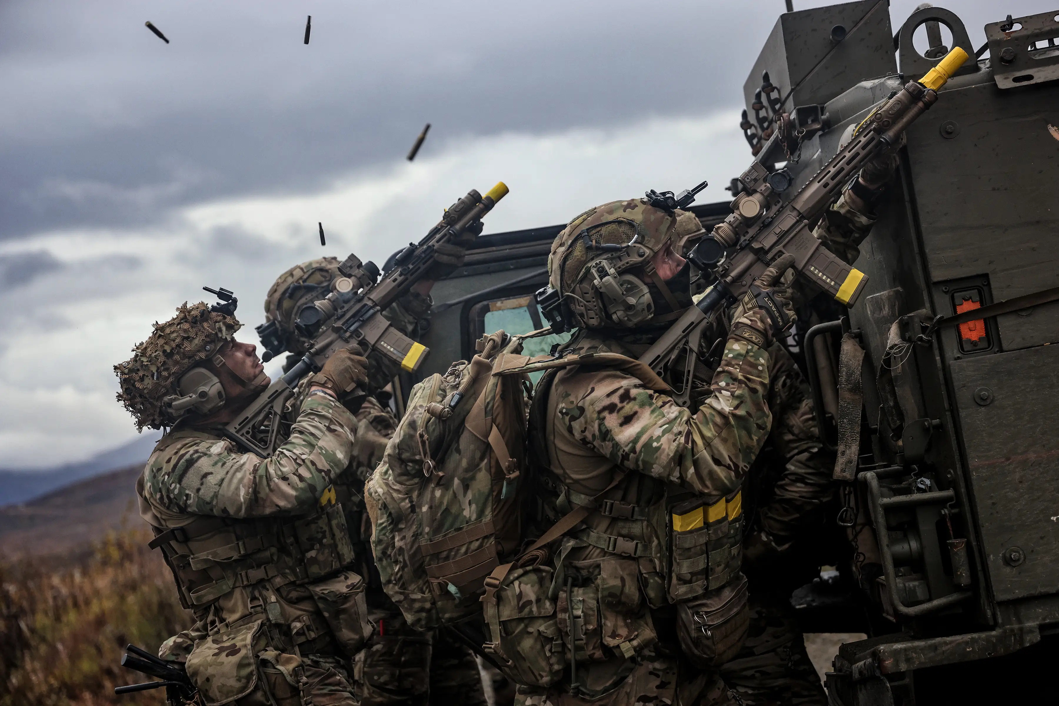 Three Royal Marines open fire from behind cover of a military vehicle.