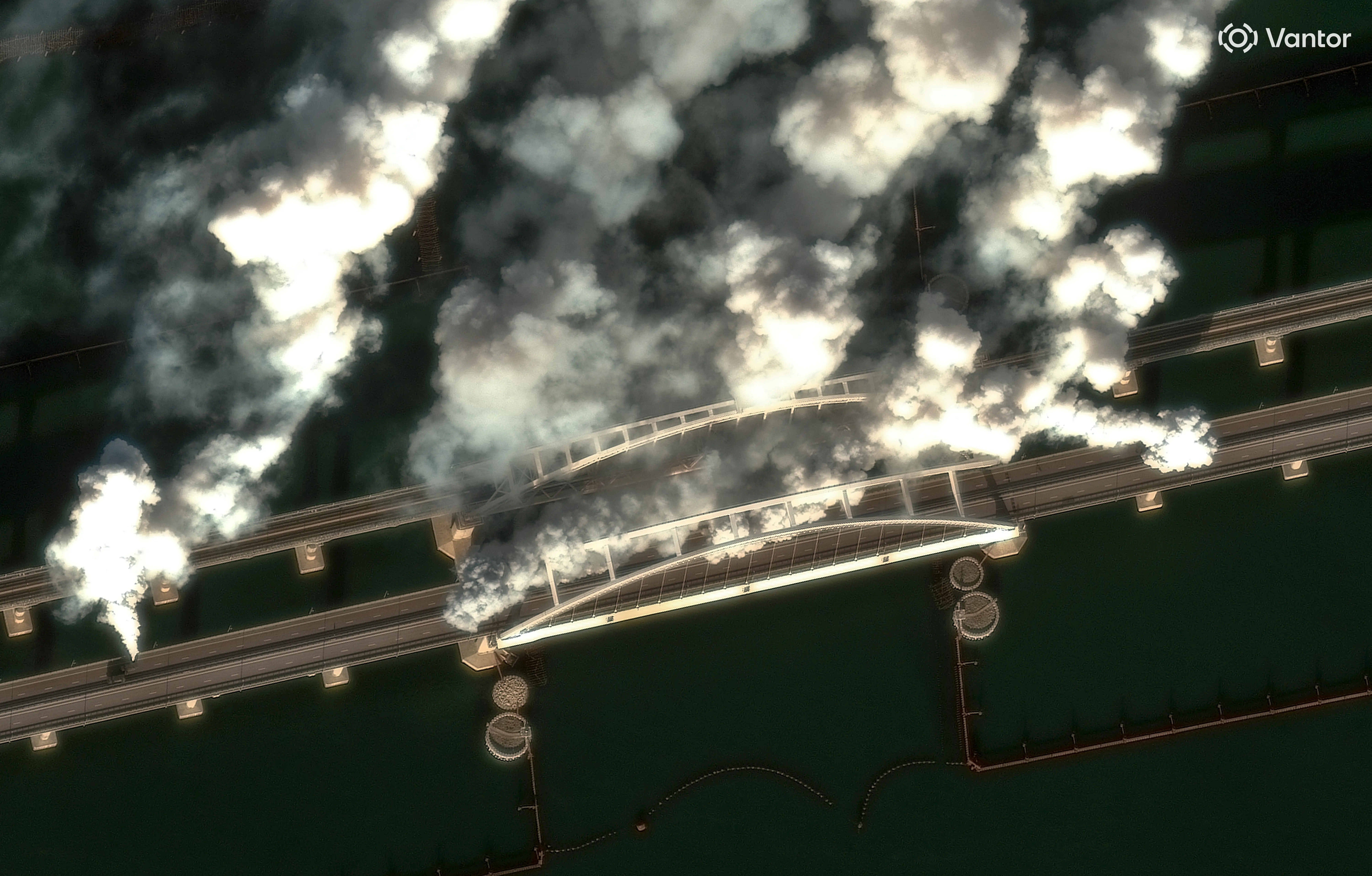 Several stacks of white and grey smoke rise from a bridge.
