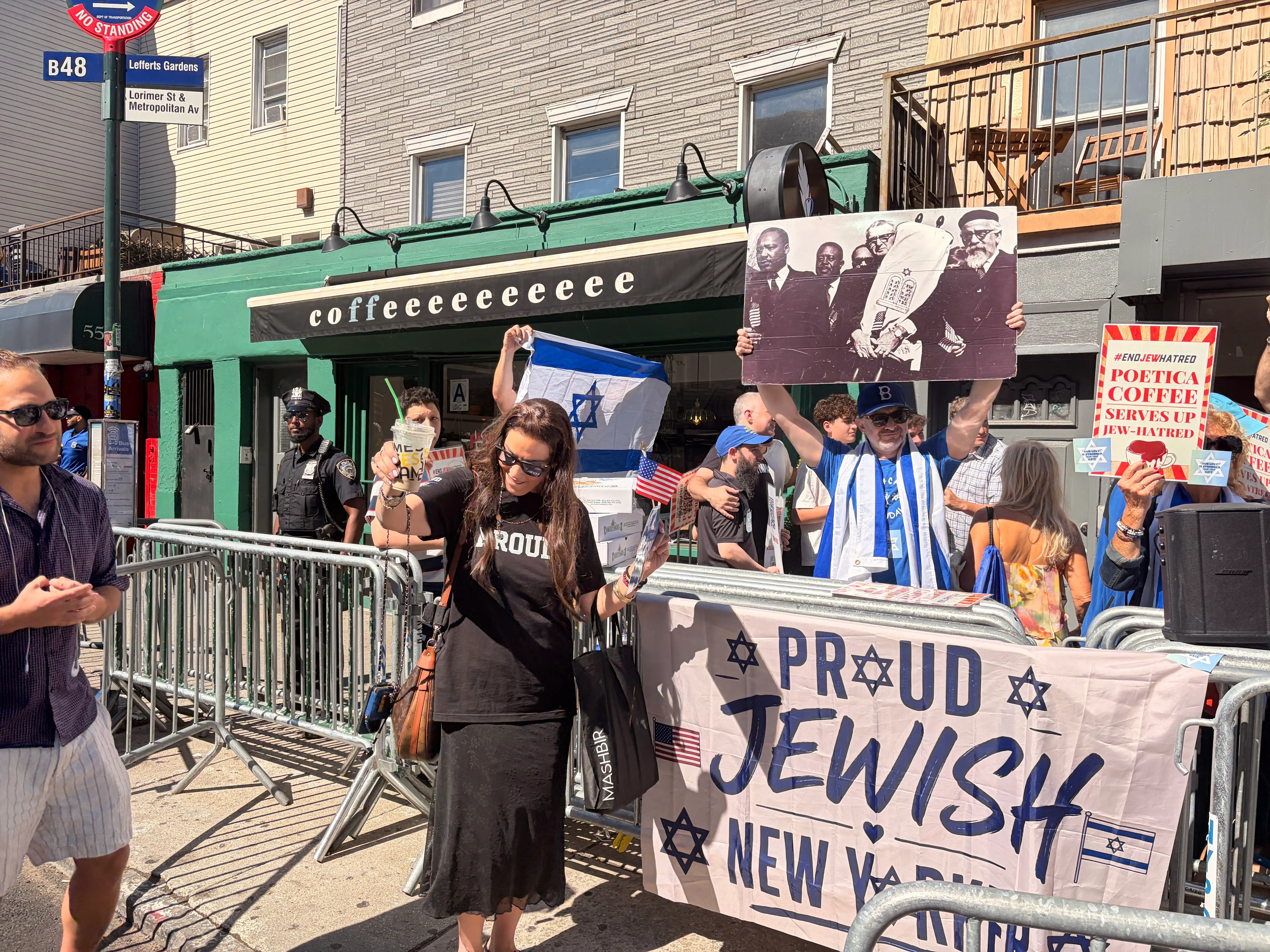 A group of people holding American and Israeli flags and protest signs outside a New York City coffee shop.
