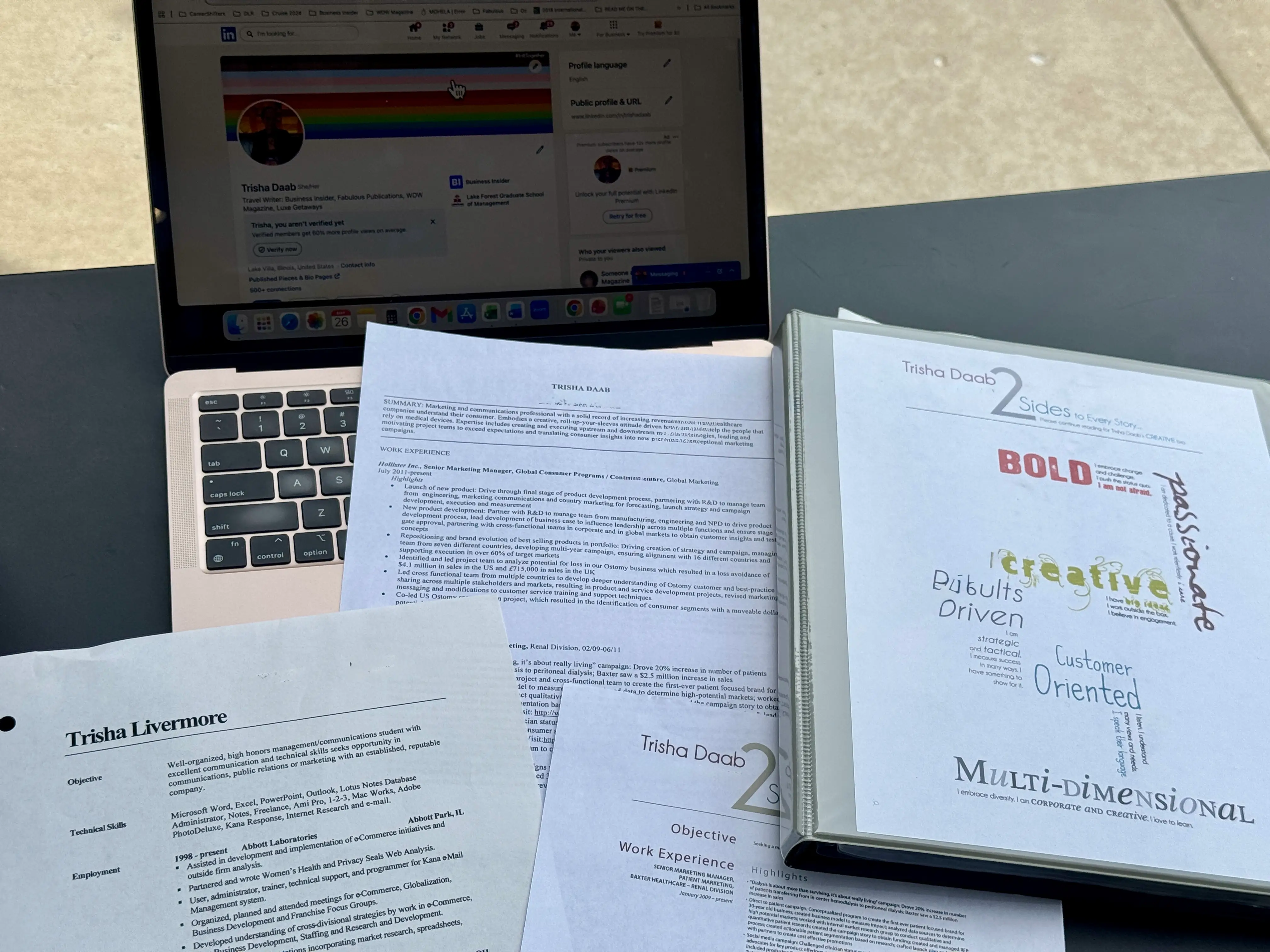 A collection of old resumes rest on a laptop.