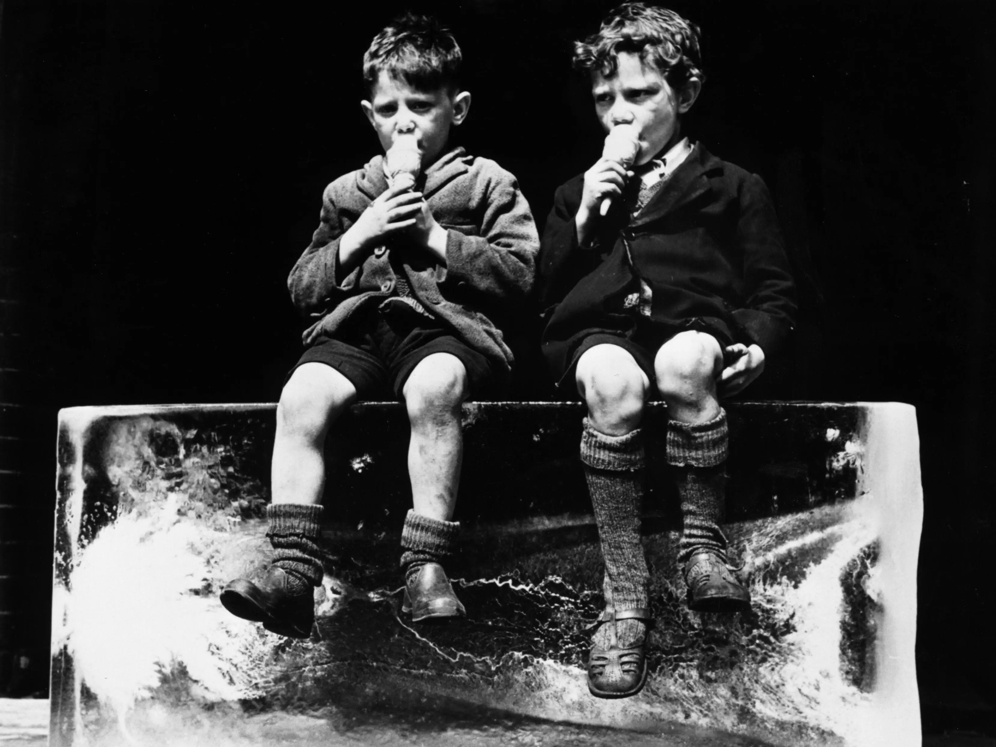 Two children eat ice cream on a block of ice