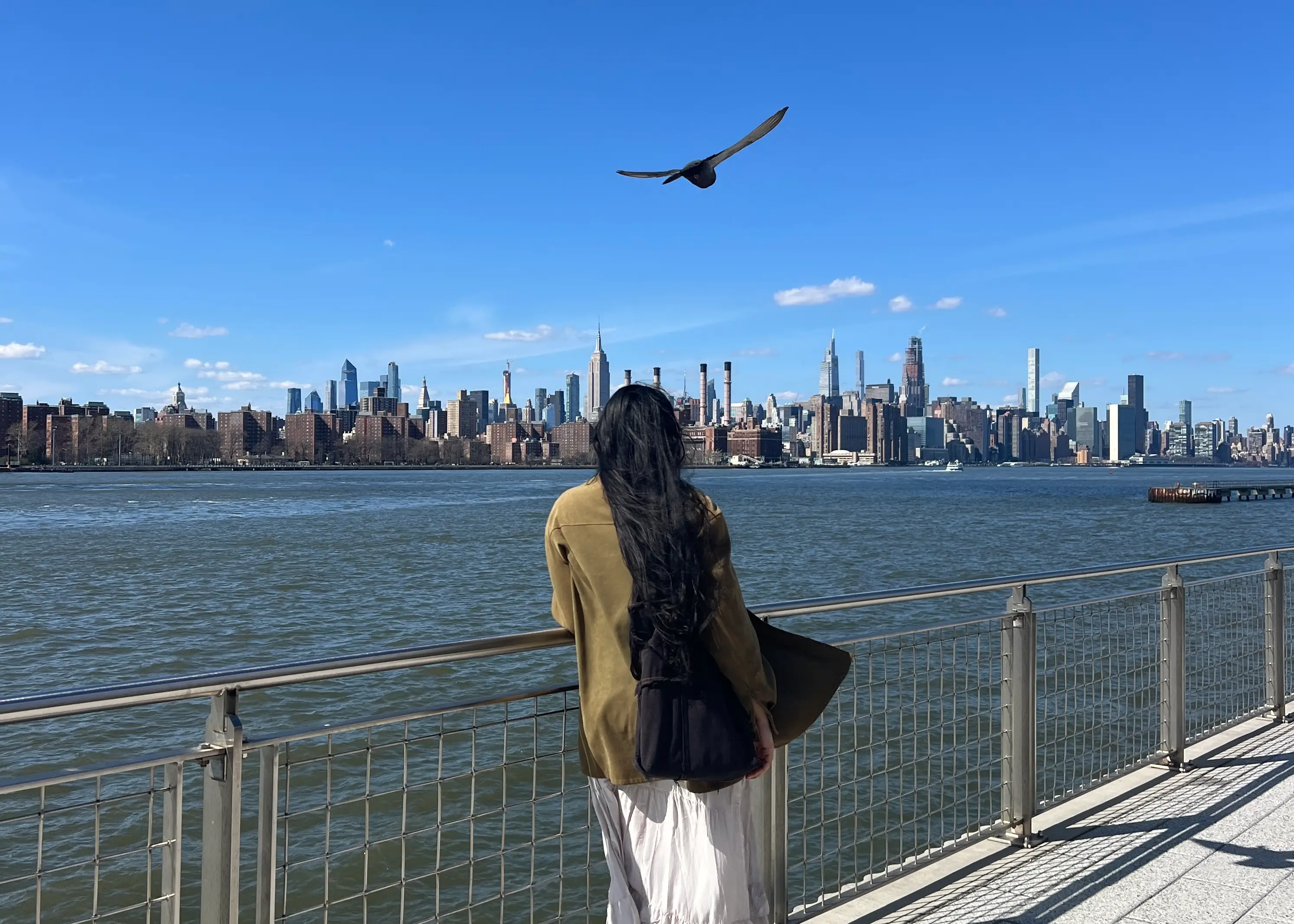 Woman leaning on railing looking toward NYC skyline