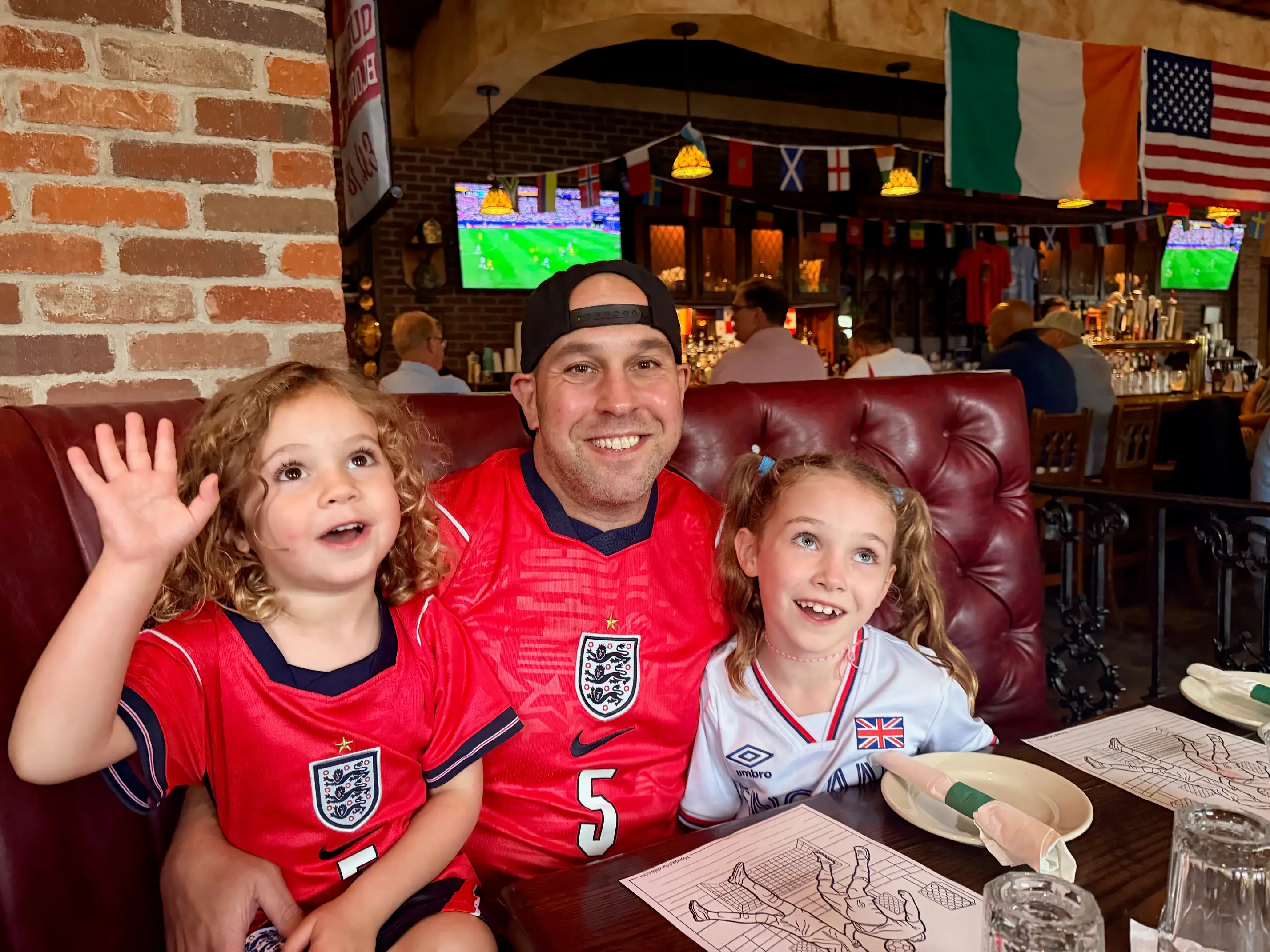 A dad is sitting in a bar wearing a soccer uniform with his two young children.