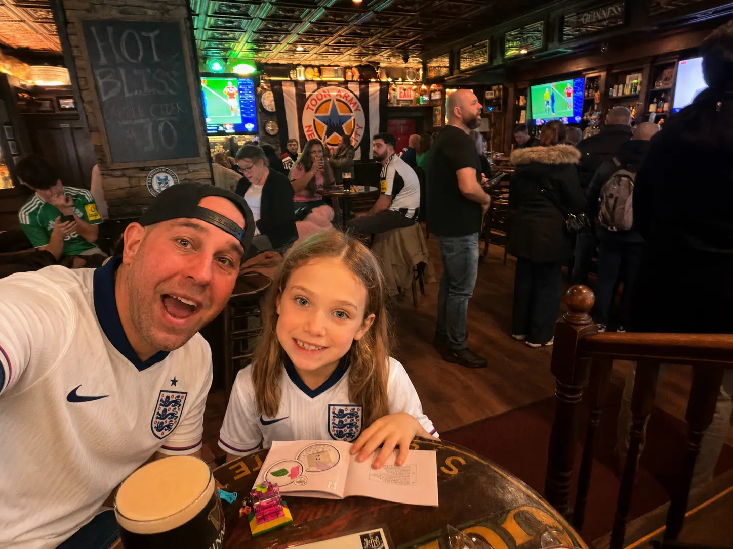 A dad in a bar with his daughter wearing soccer jerseys.